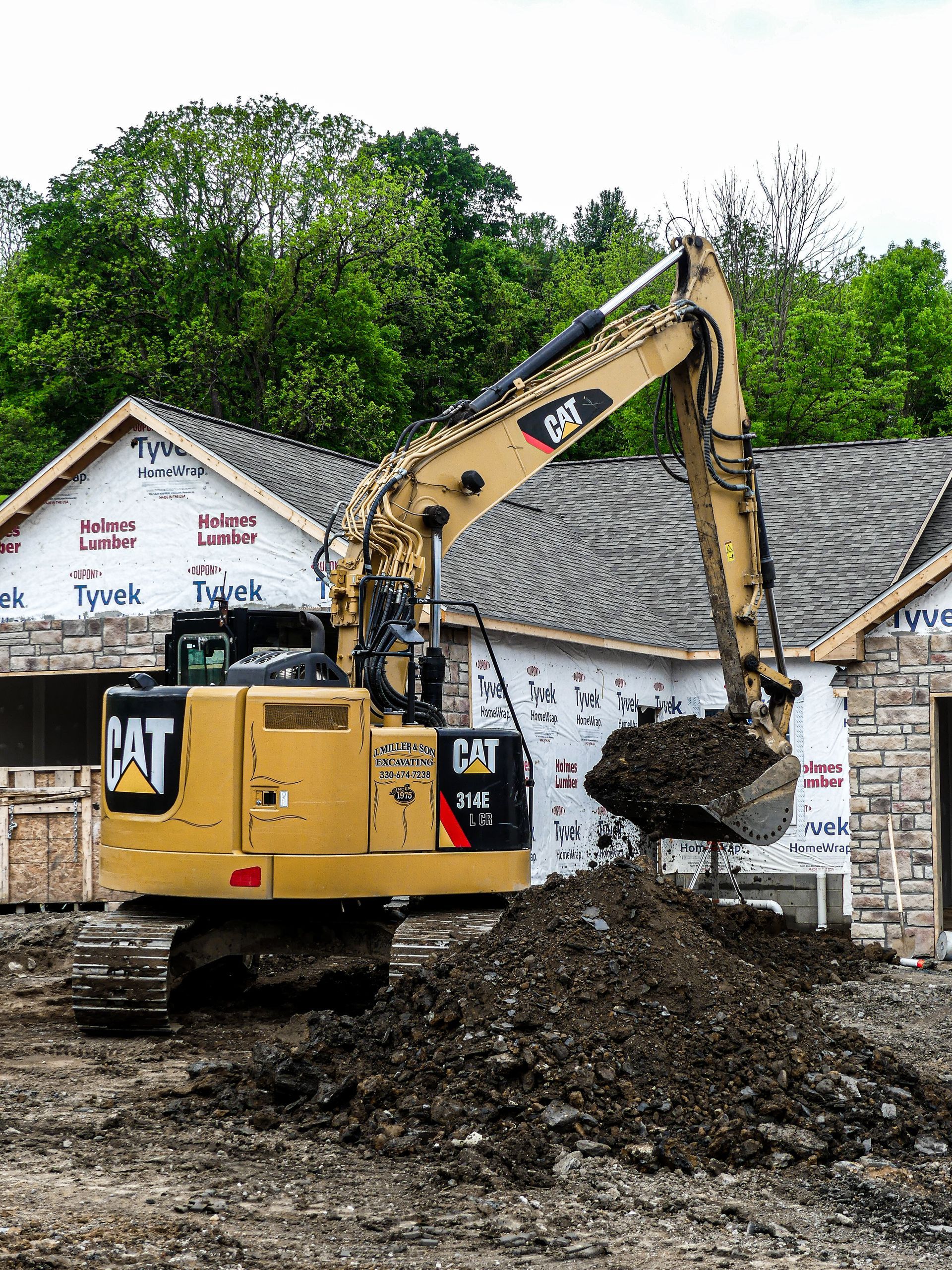 Yellow Caterpillar excavator at a construction site, scooping dirt. Houses under construction in the background.