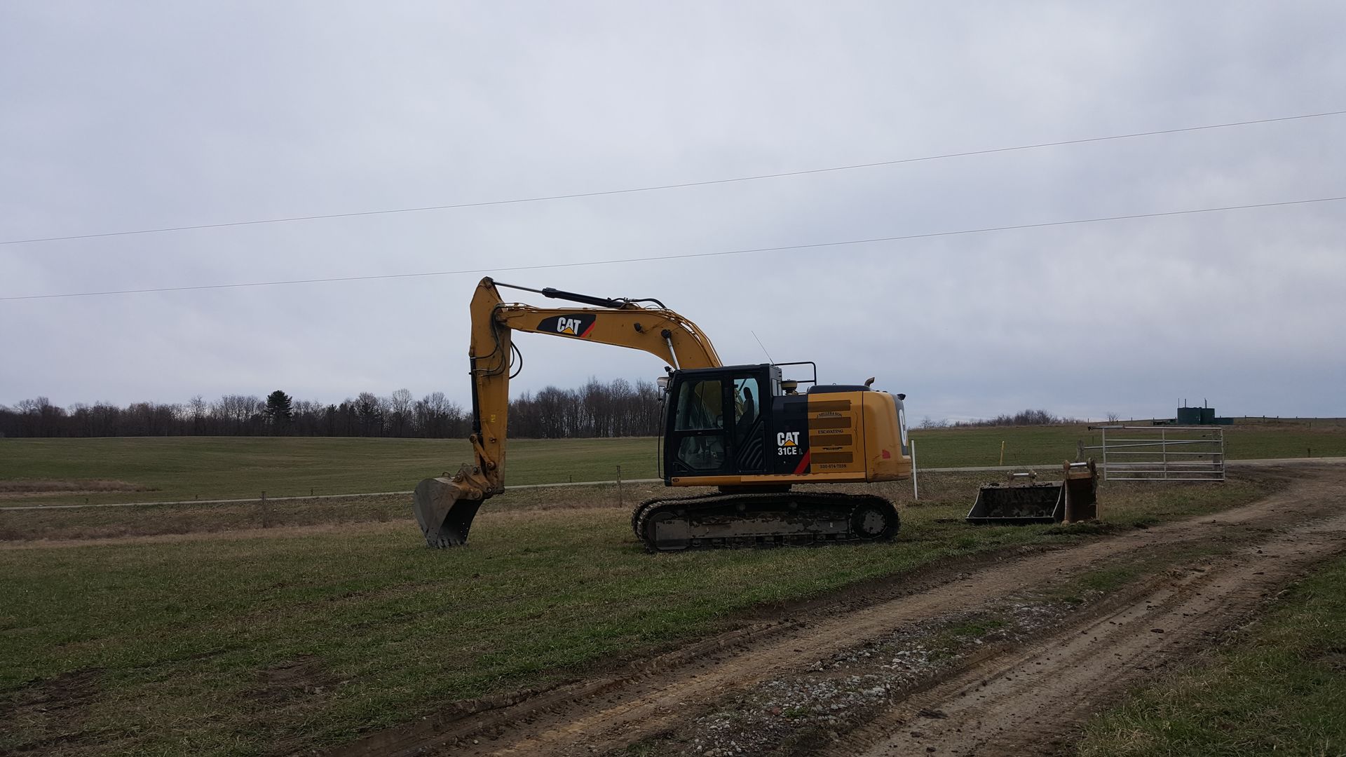 Yellow Caterpillar excavator on a field, preparing ground. A flock of birds flies in a cloudy sky.
