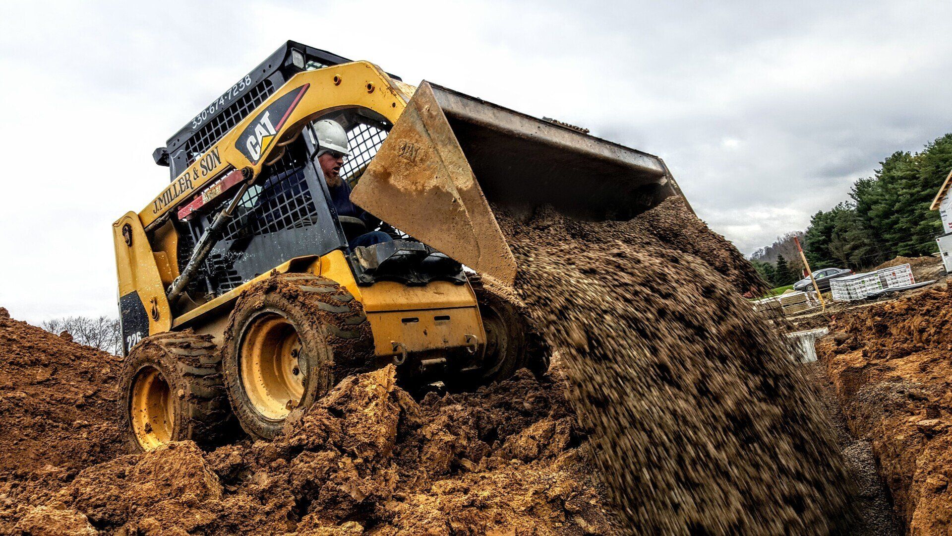 Yellow skid steer loading dirt into a pile, outdoors.