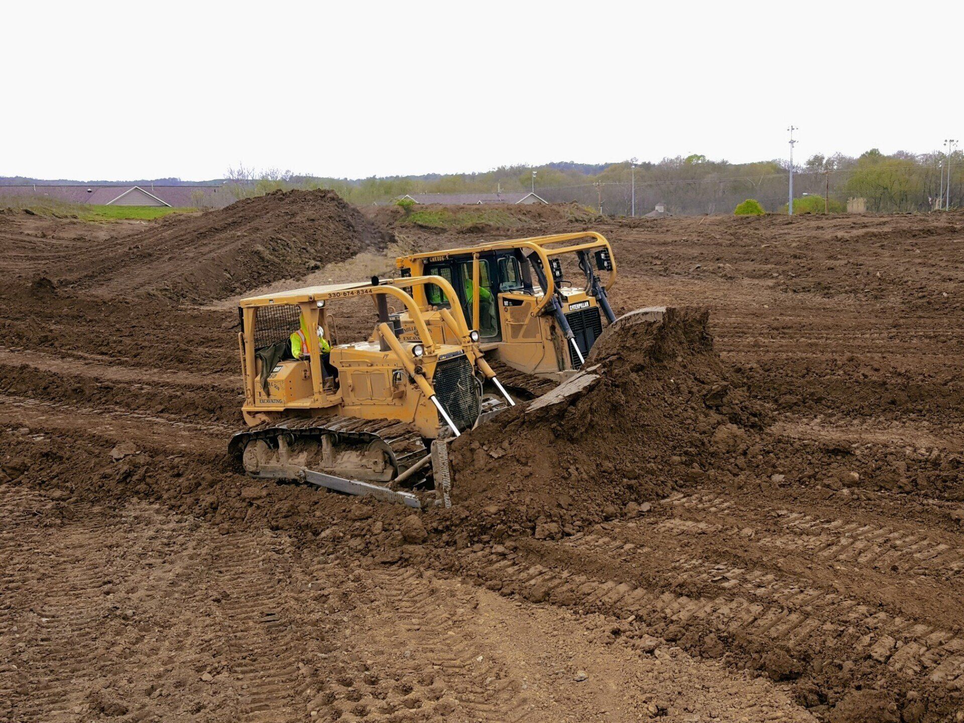 Three yellow bulldozers pushing dirt in an open field during construction.