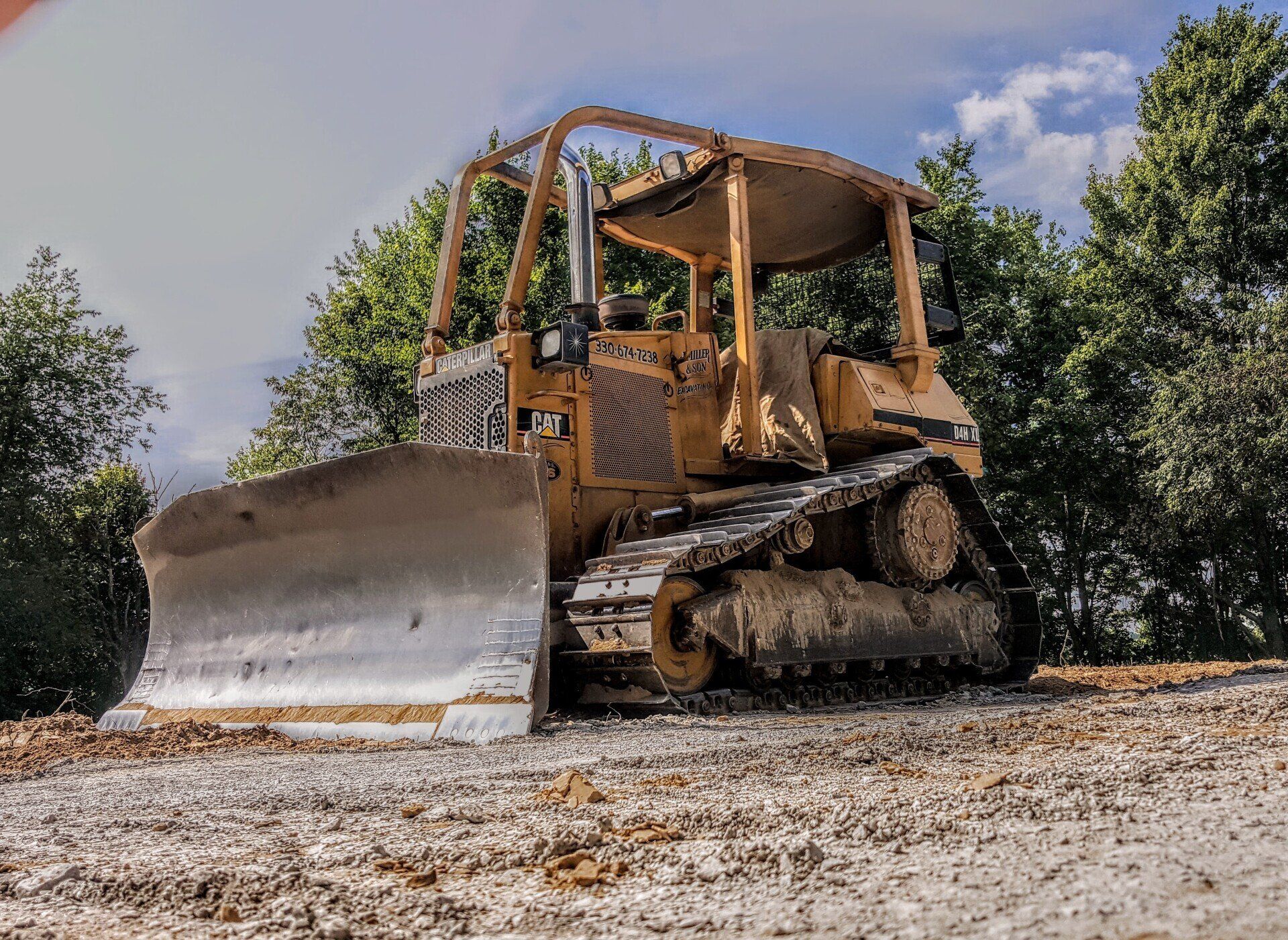 Yellow bulldozer on a gravel surface, surrounded by trees.