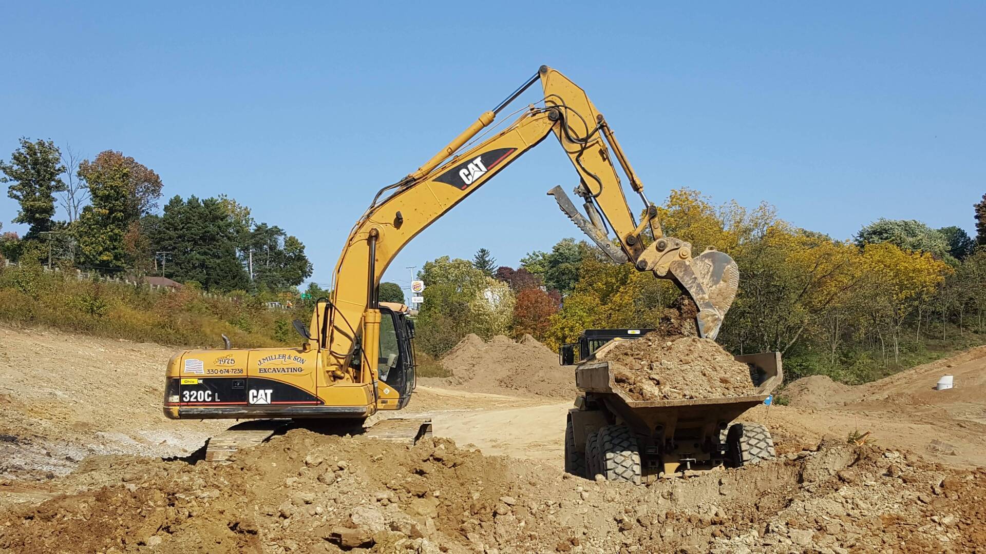 Yellow excavator filling a small dump truck with dirt on a construction site.