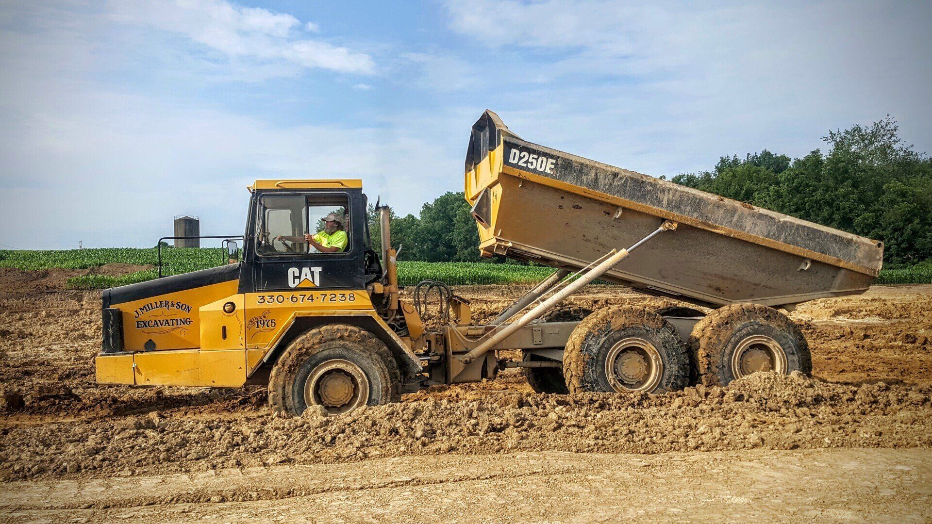Yellow Caterpillar dump truck stuck in mud, bed raised, in a construction site.
