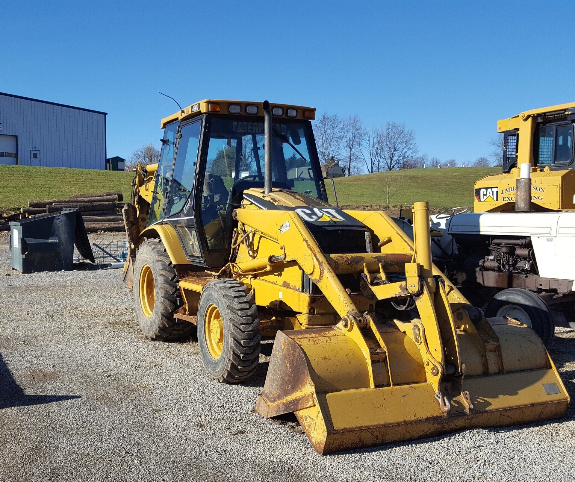 Yellow Caterpillar backhoe in gravel lot under blue sky.