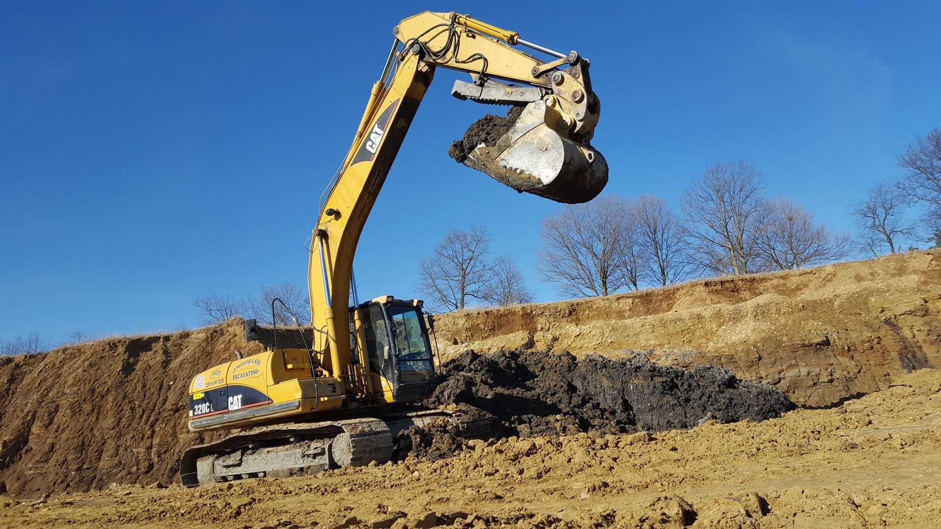 Yellow excavator digging earth on a construction site; blue sky in background.