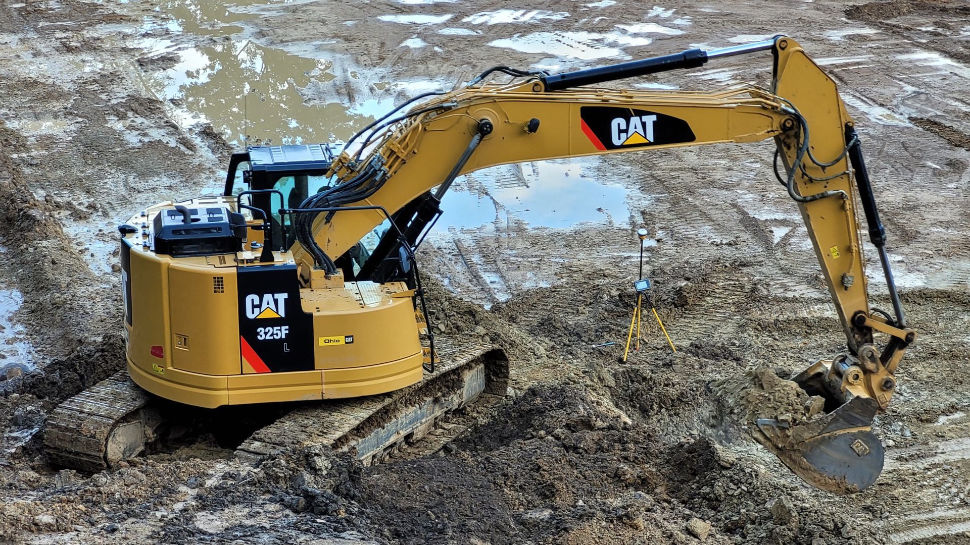 Yellow Caterpillar excavator in muddy terrain.