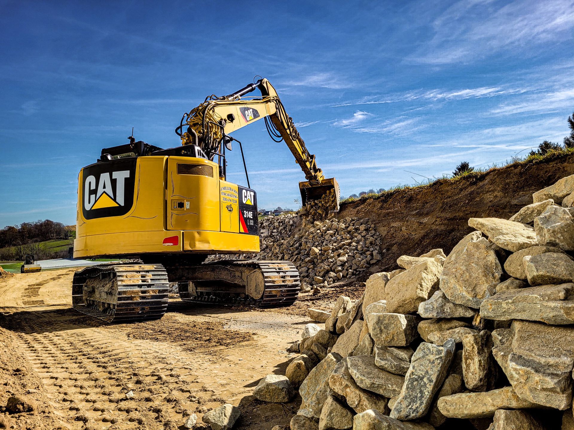 Yellow Caterpillar excavator digging earth on a construction site with rocks and a blue sky.