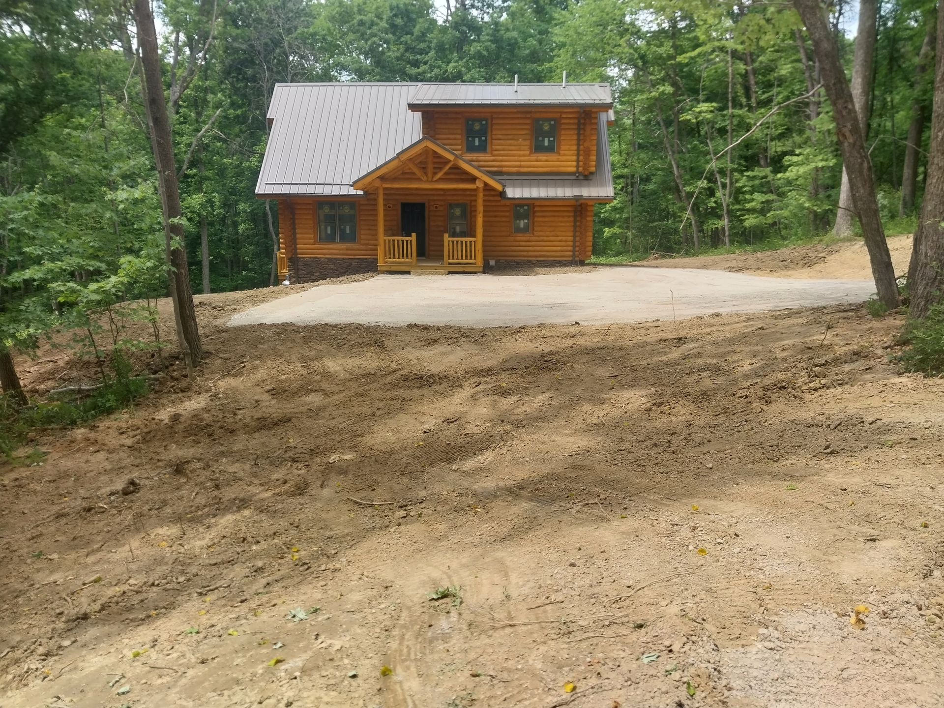 Log cabin with a gravel driveway surrounded by trees.