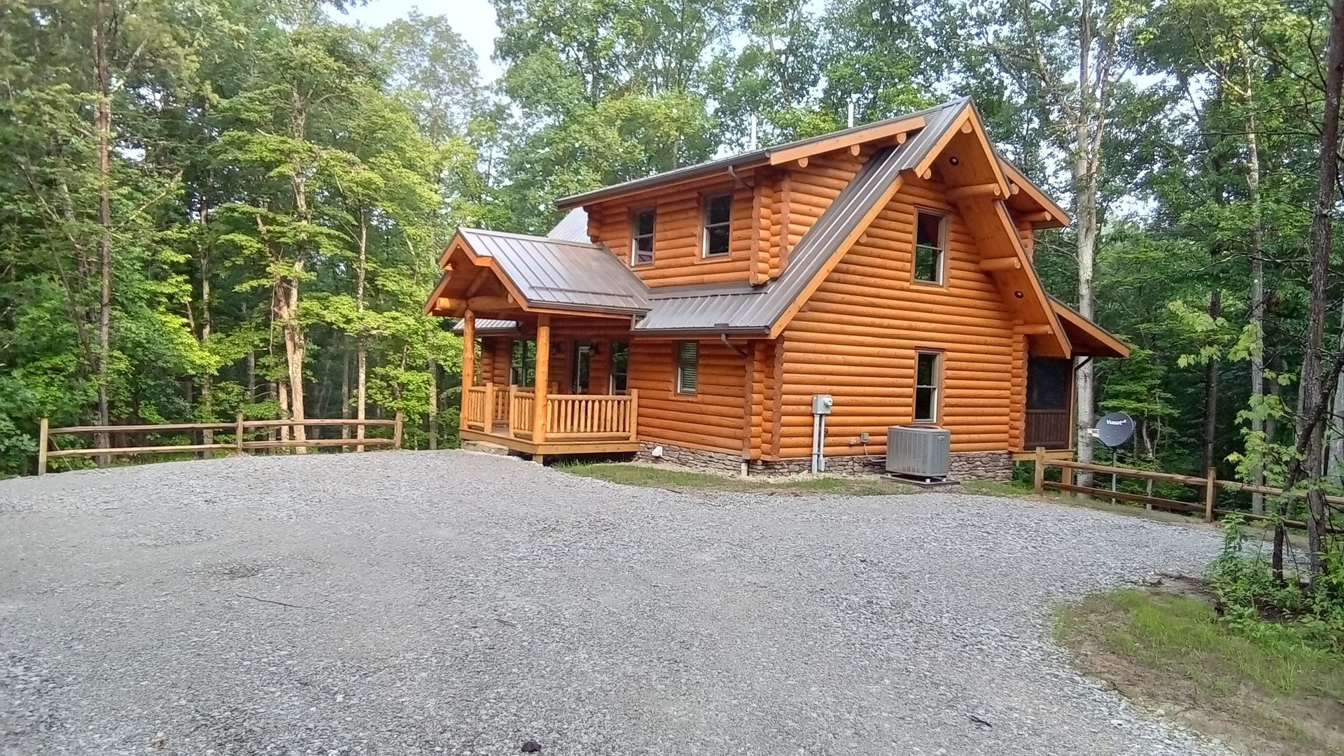 A log cabin with a gravel driveway, surrounded by trees.