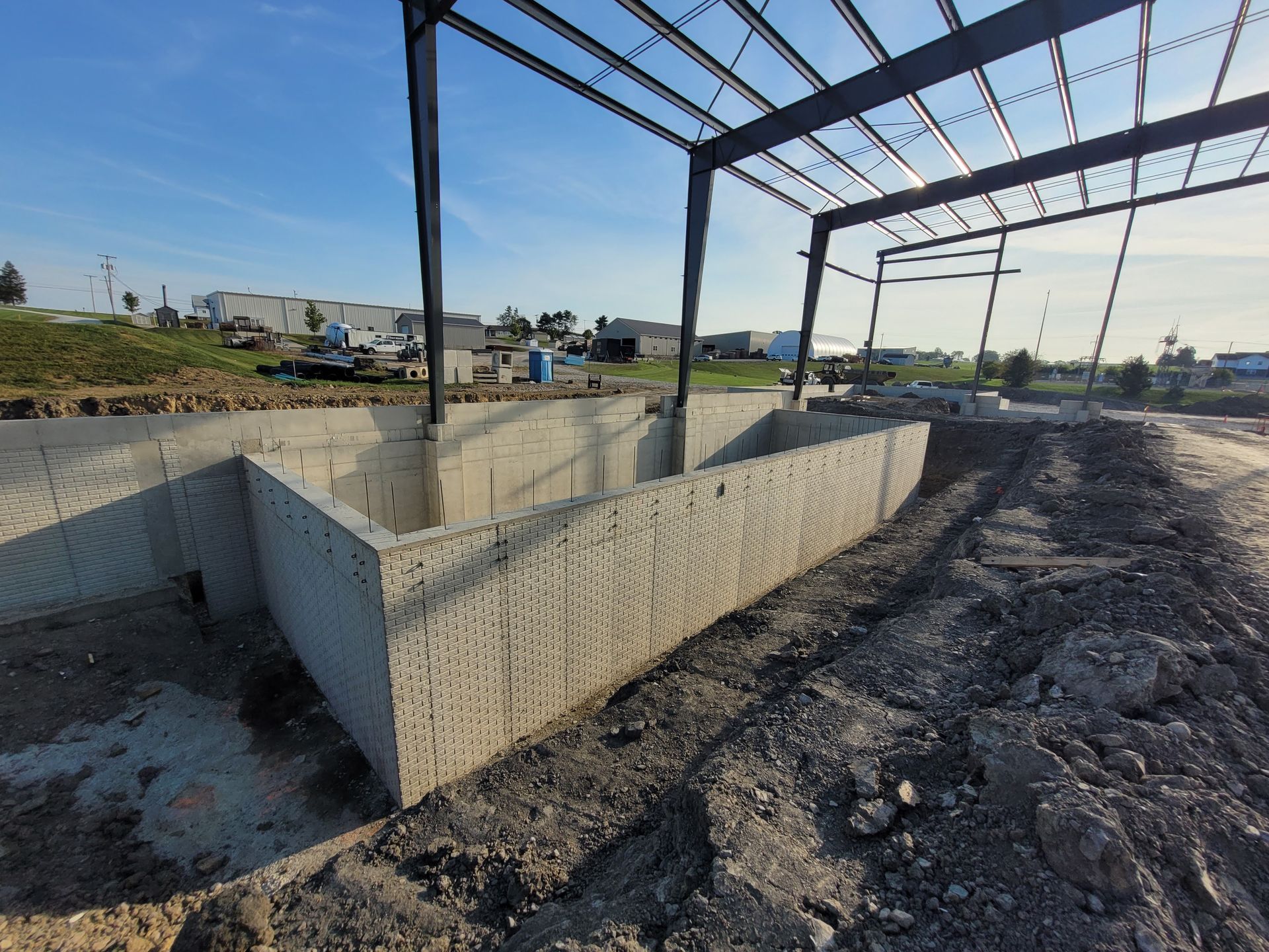 Construction site: concrete foundation and steel framework under a blue sky.