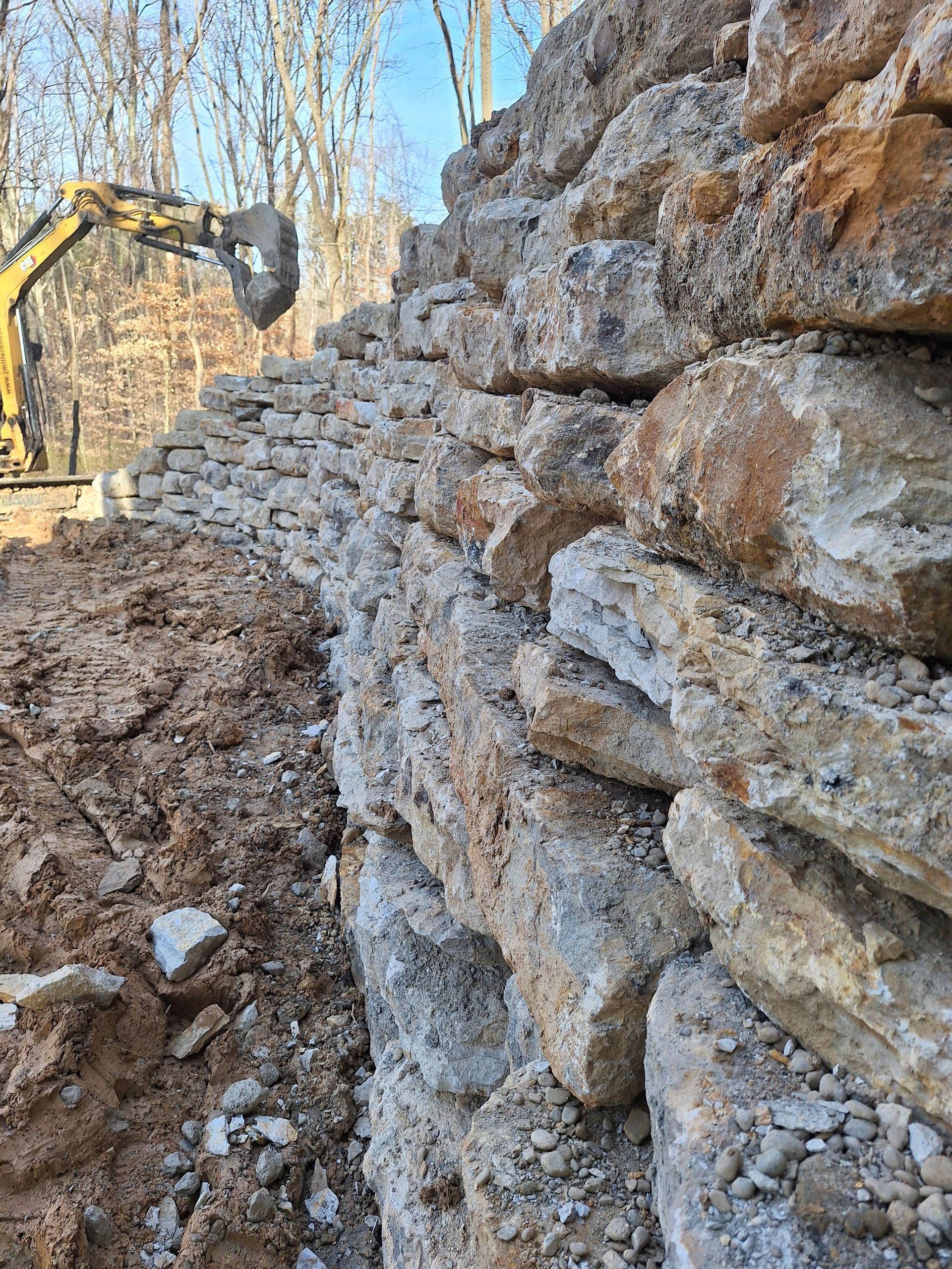 Stone retaining wall construction with an excavator in the background.