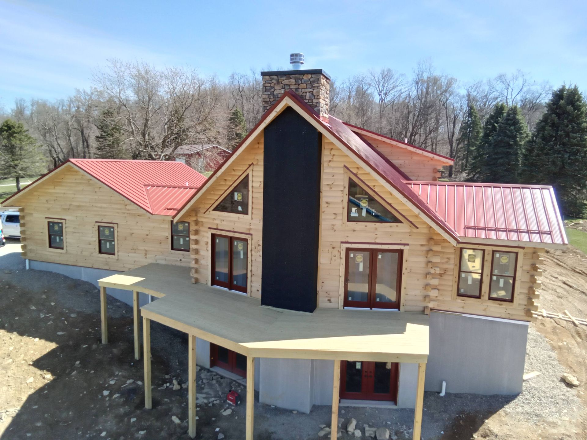 Log cabin home under construction with a red metal roof and deck.