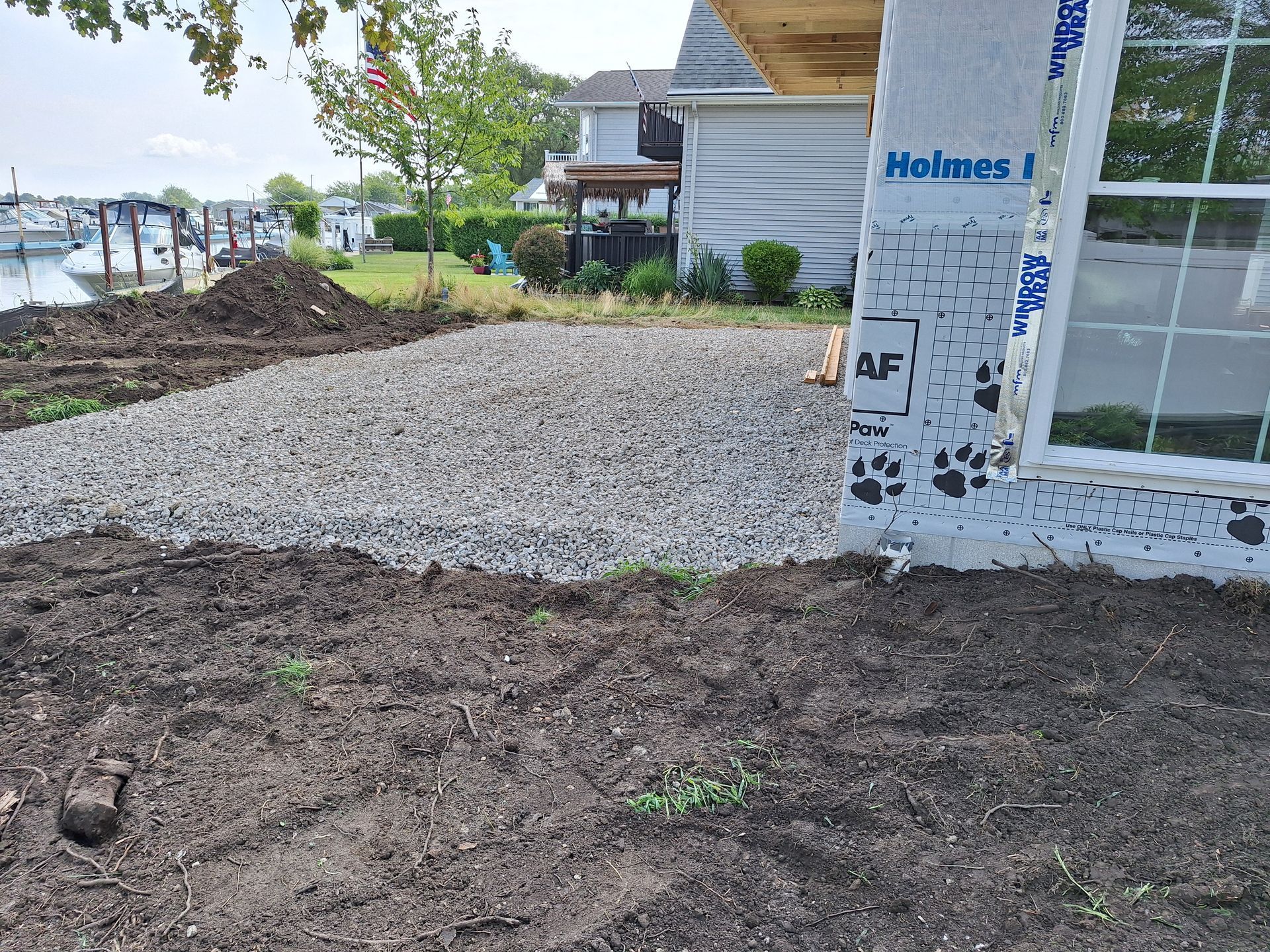 Gravel and dirt patio construction next to a building, by a harbor.