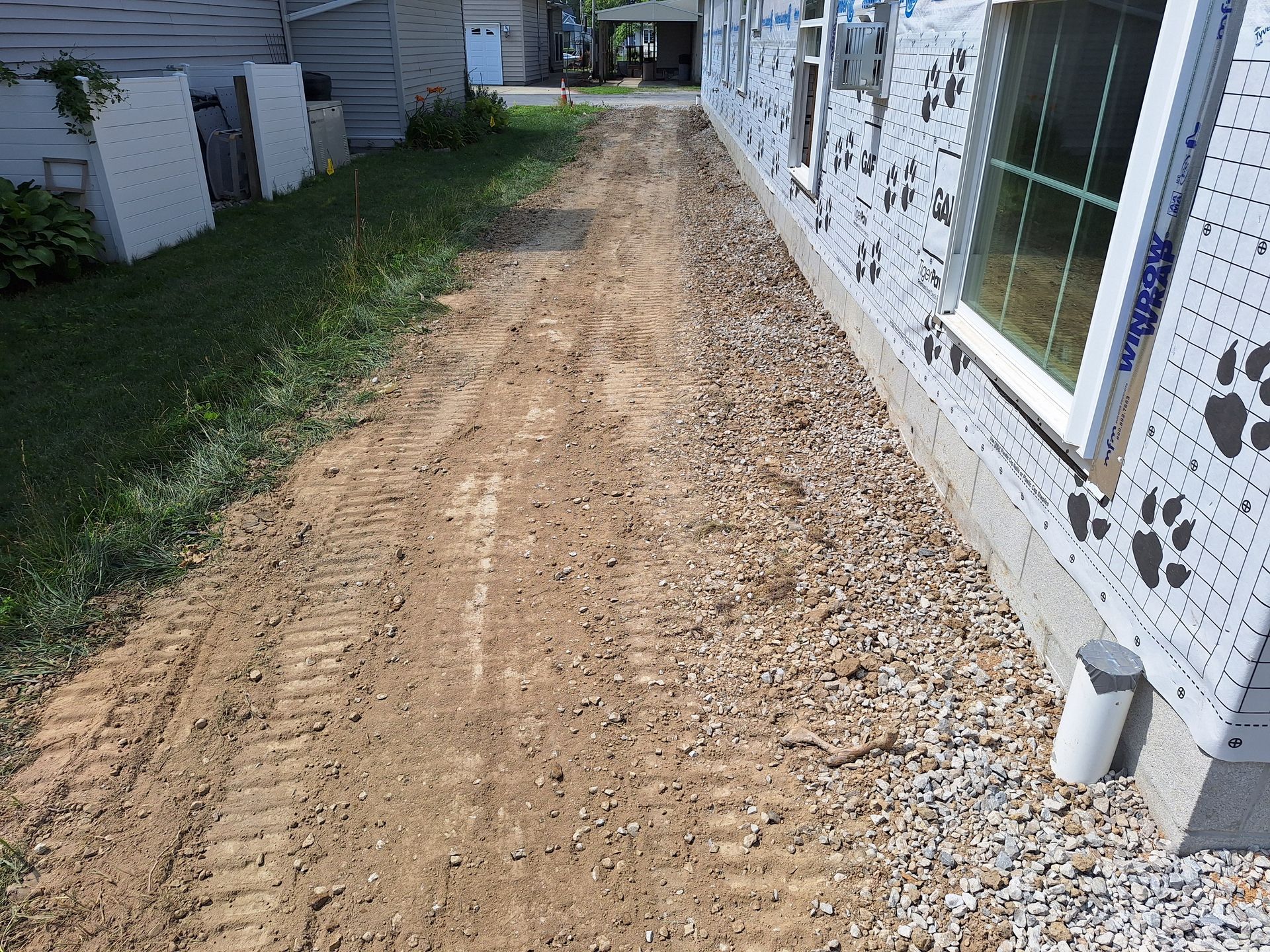 Dirt and gravel path beside a building with unfinished siding and a window.