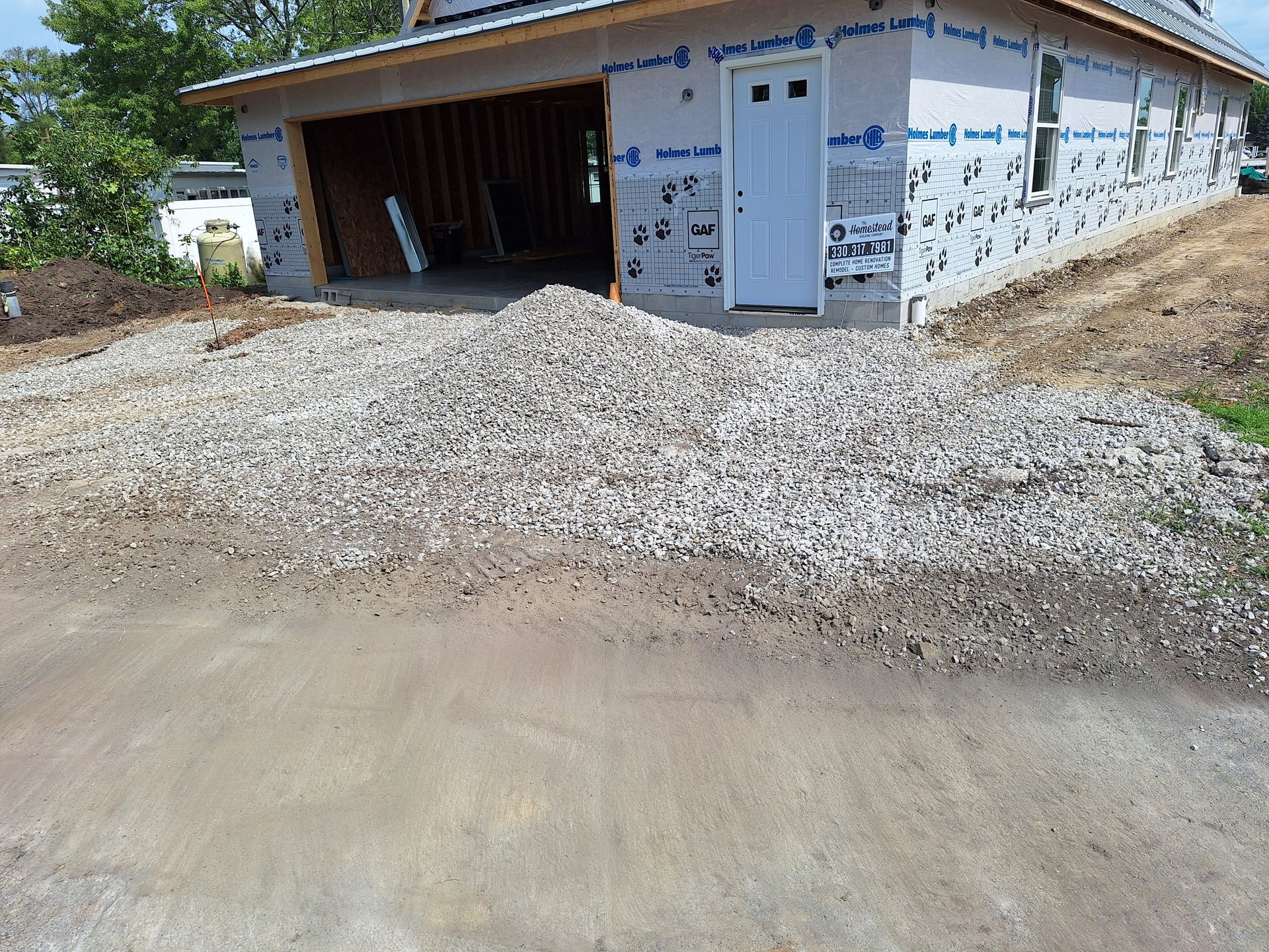 Gravel pile in front of a partially constructed garage with a white door and wood framing.