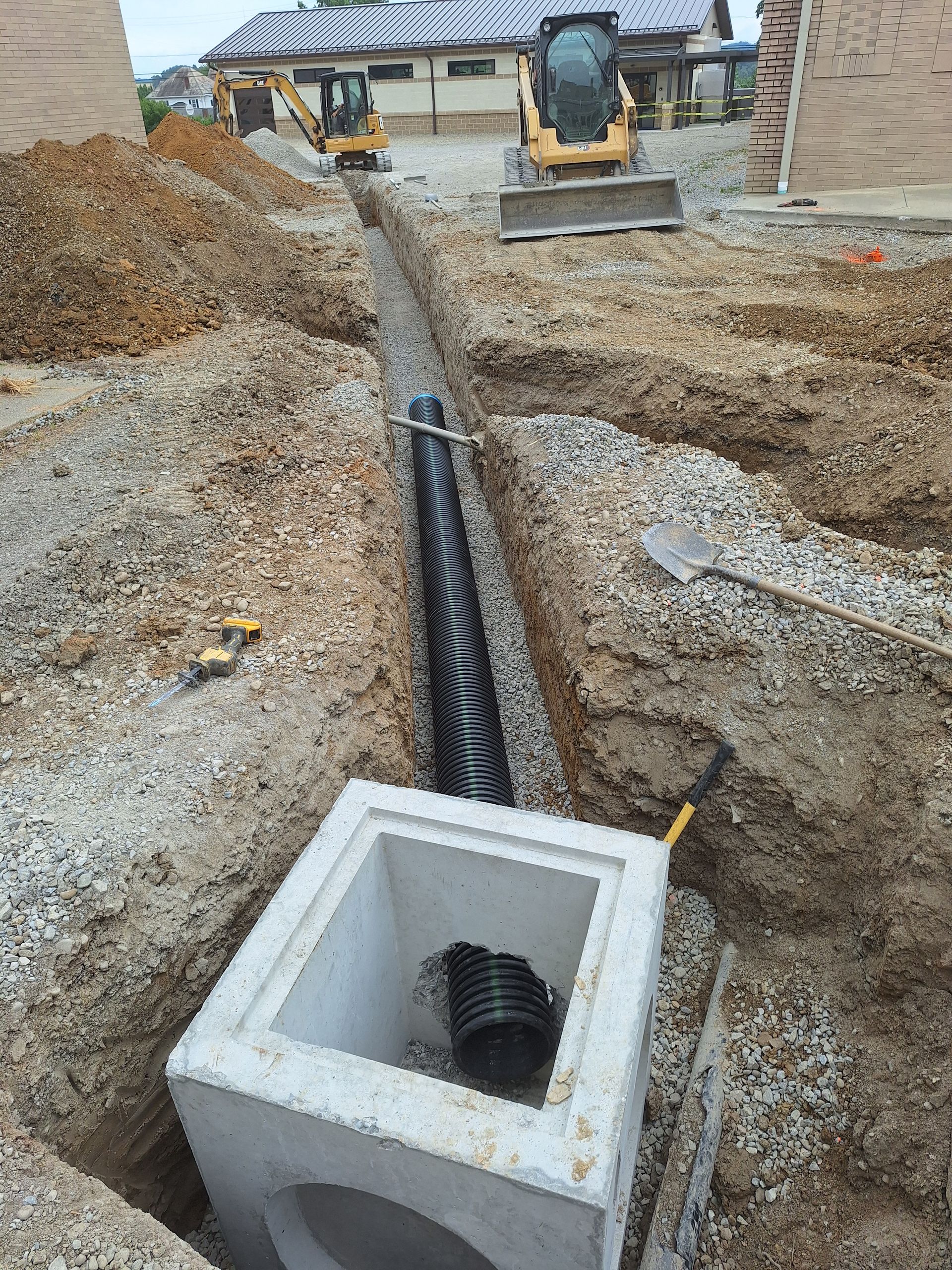 Construction site: Excavation for a drainage system with a pipe, manhole, and heavy machinery.