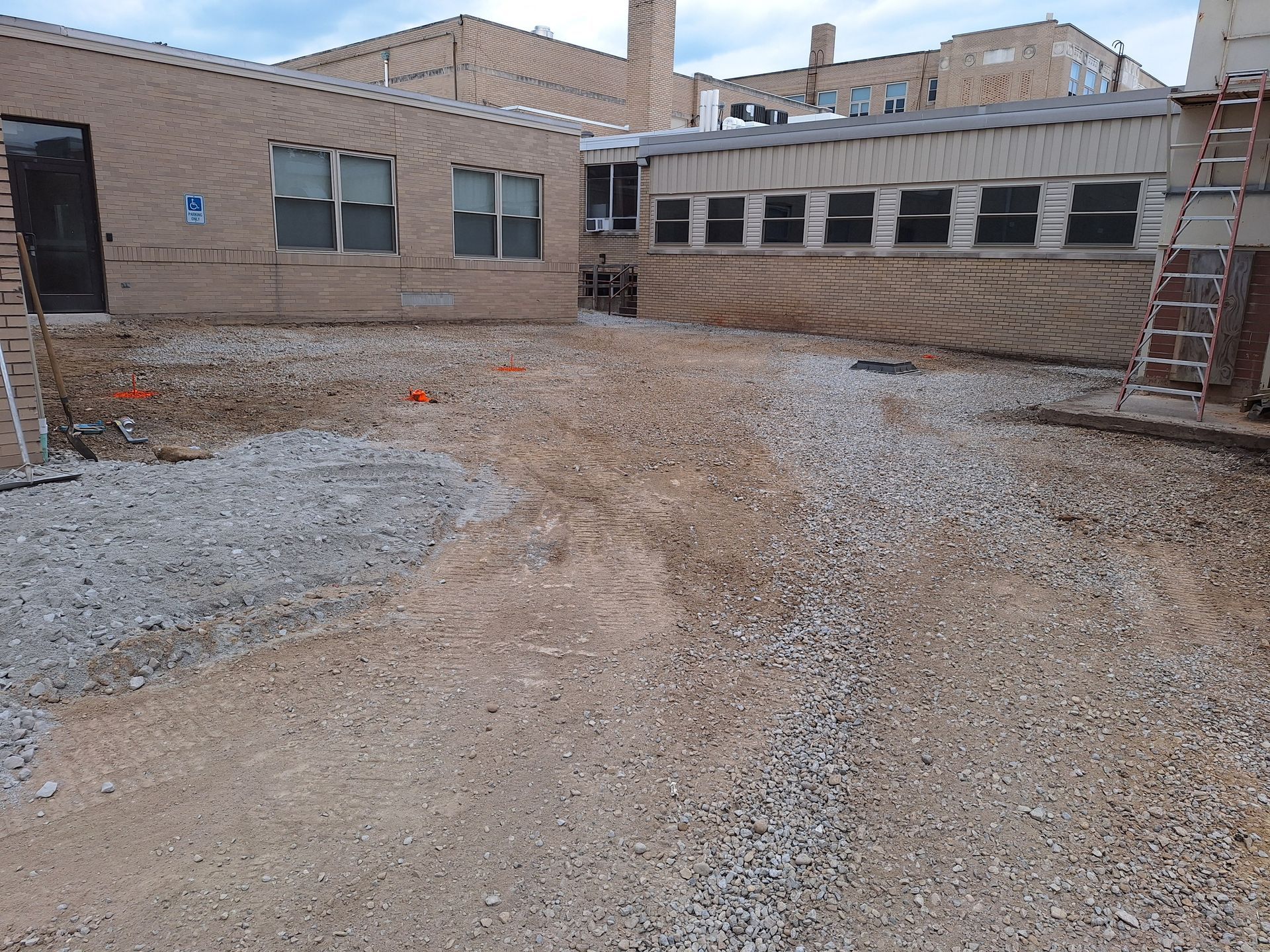 Exterior view of a gravel yard with buildings in the background. Construction cones and equipment visible.