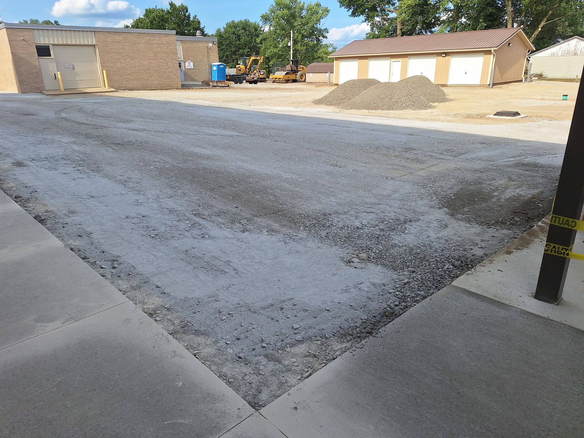 Gravel surface in front of a building, with construction equipment in the background. Sunny day.