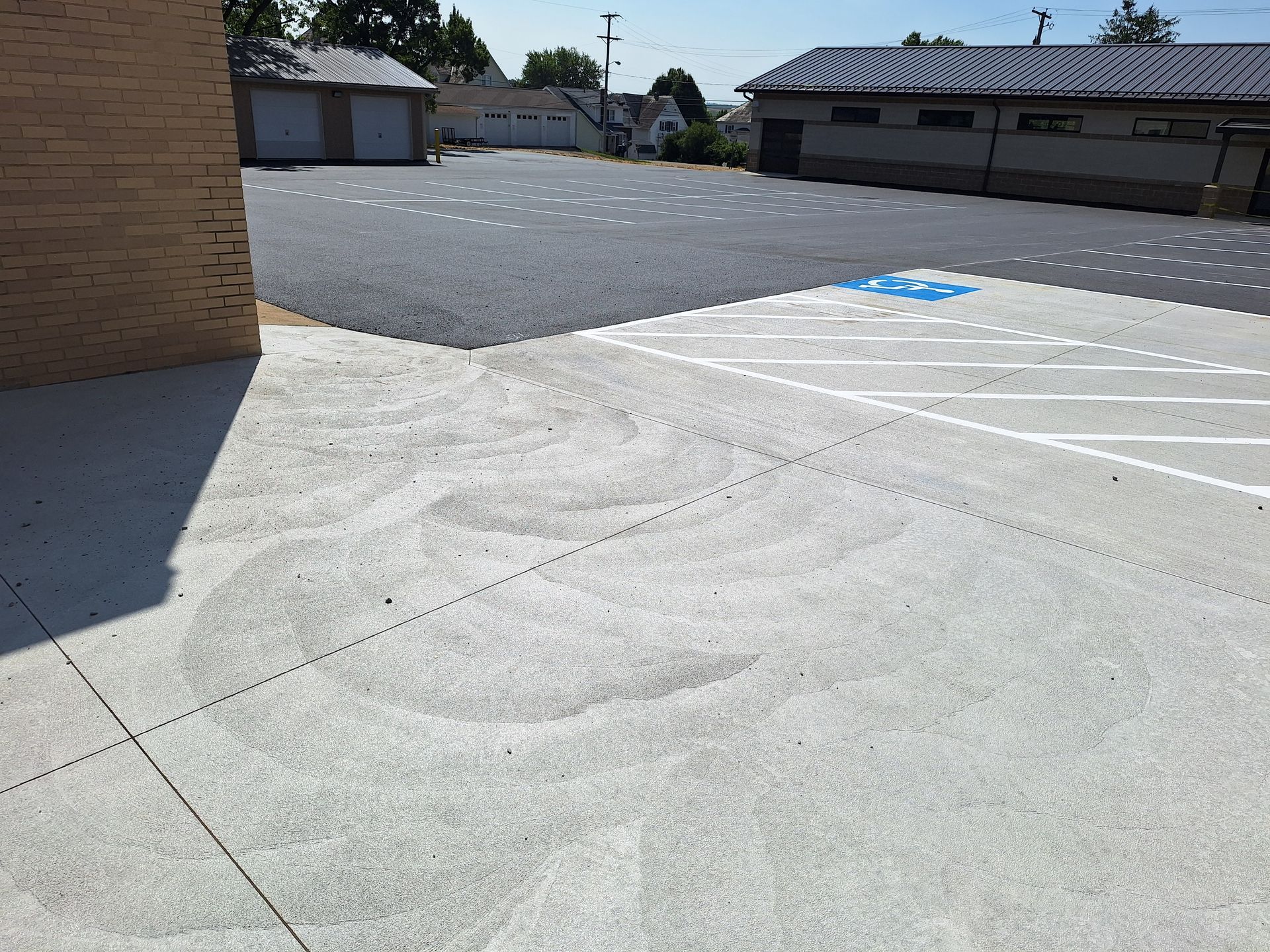 Concrete parking lot with marked spaces, building in the background on a sunny day.