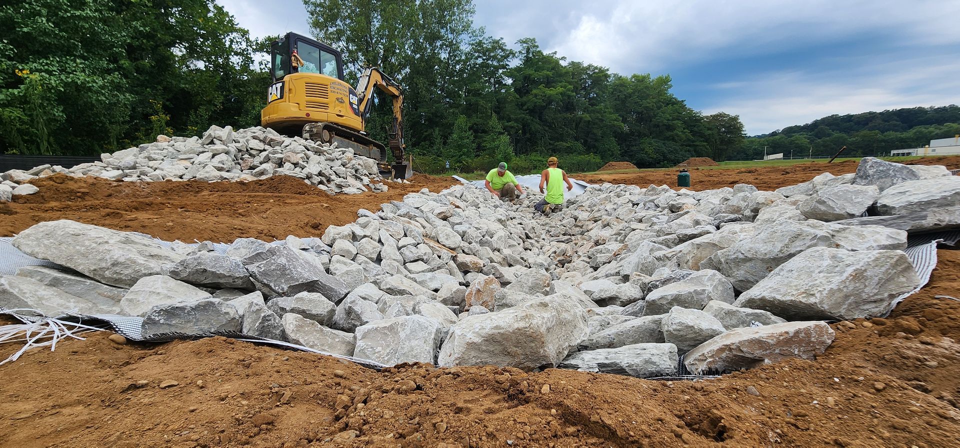 Construction site with an excavator and workers; concrete debris on the ground.