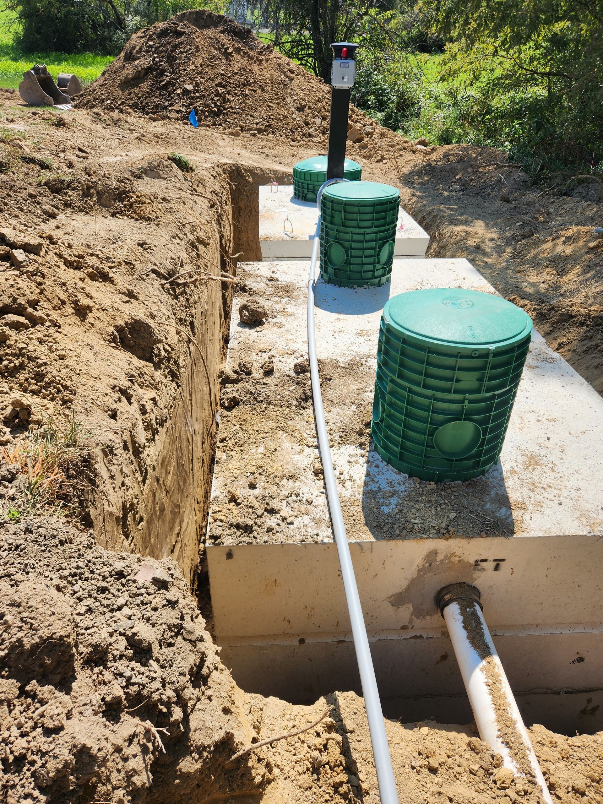 Construction site: septic tanks and piping in a dug trench, with green access covers.