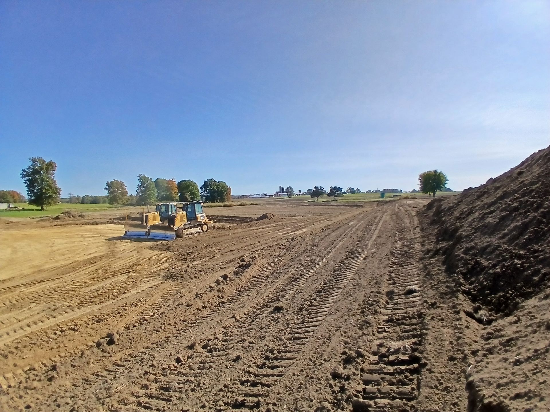 Bulldozer on muddy ground, preparing land under a blue sky.