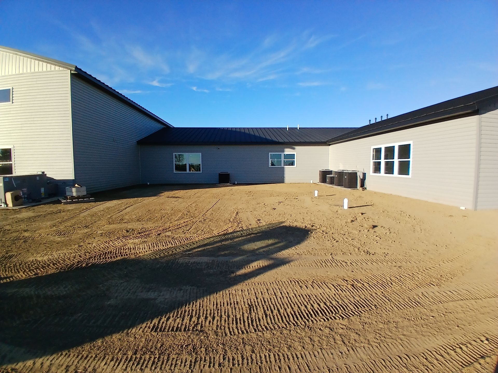 Backyard of a building under construction, featuring light gray siding, a blue sky, and packed dirt.