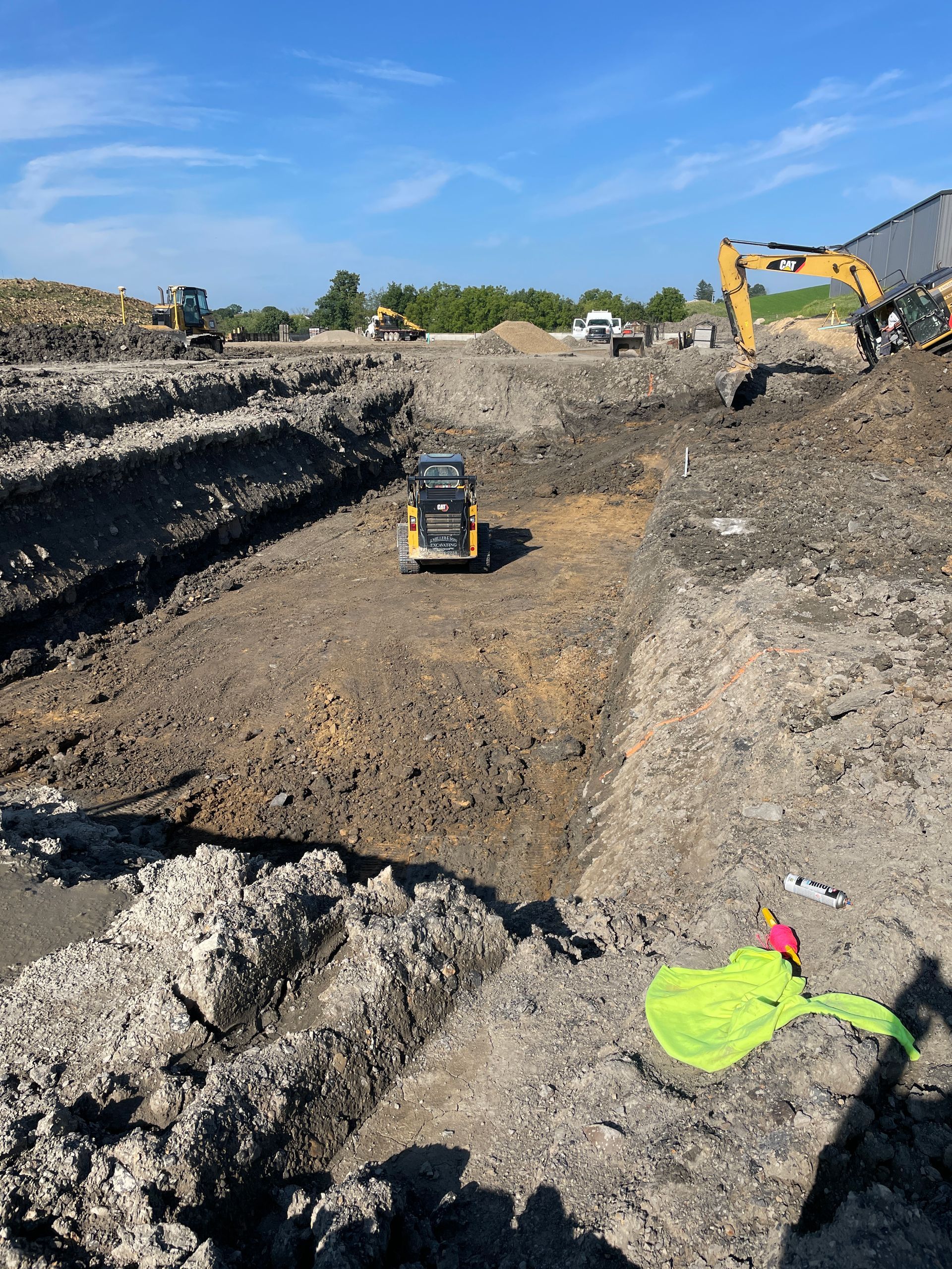 Construction site with trench and heavy machinery. Yellow and black excavators and a compact track loader operate.
