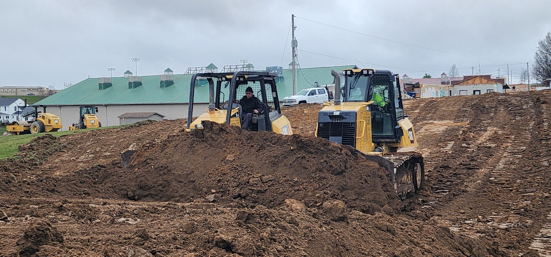 Two yellow bulldozers move dirt at a construction site on a cloudy day.