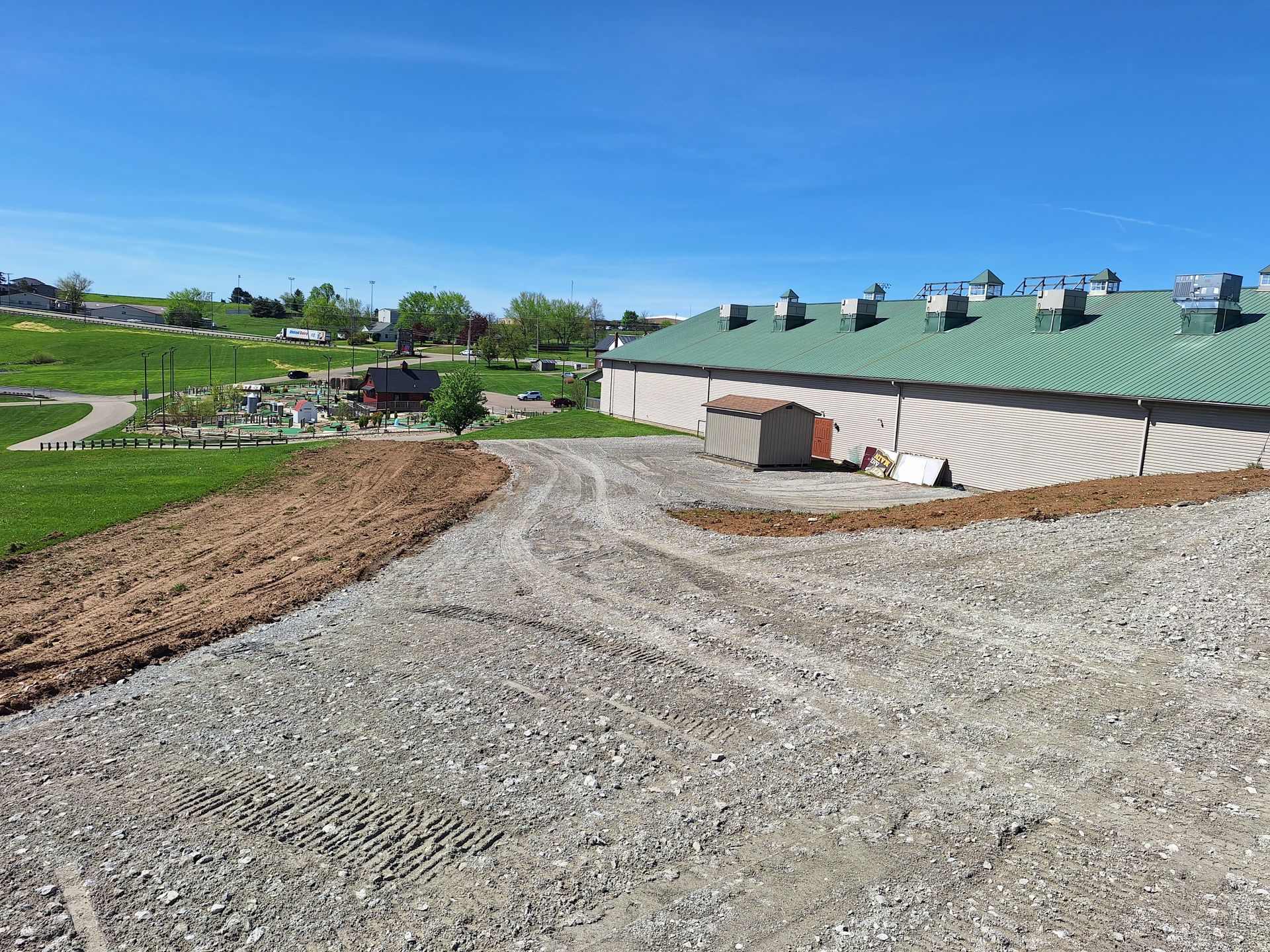 Gravel and dirt area in front of a building with a green roof under a clear blue sky.