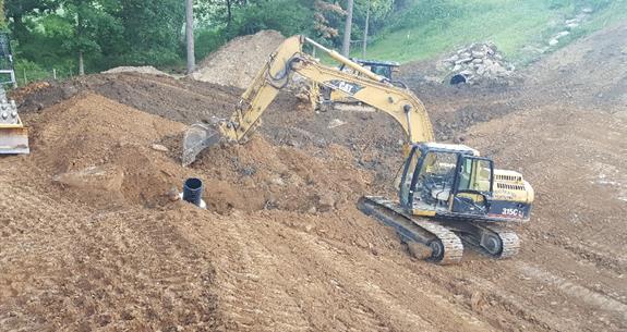 An excavator on a hillside moving earth, working on a construction project.