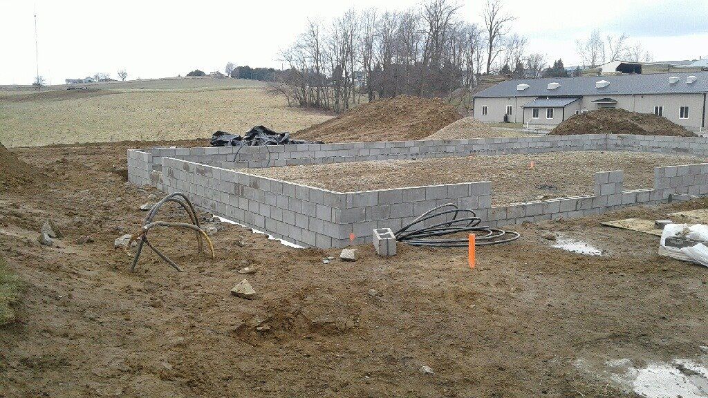 Foundation of a building under construction made of gray concrete blocks; dirt surrounds the site.
