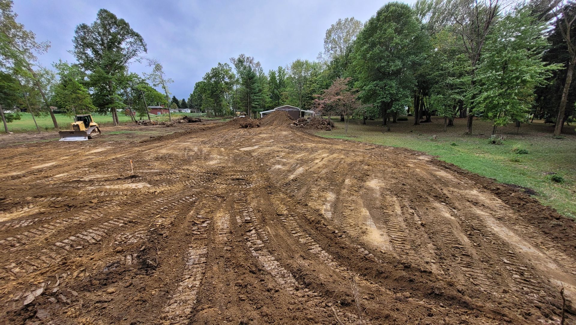 Muddy field, tilled, with trees in the background under a cloudy sky.