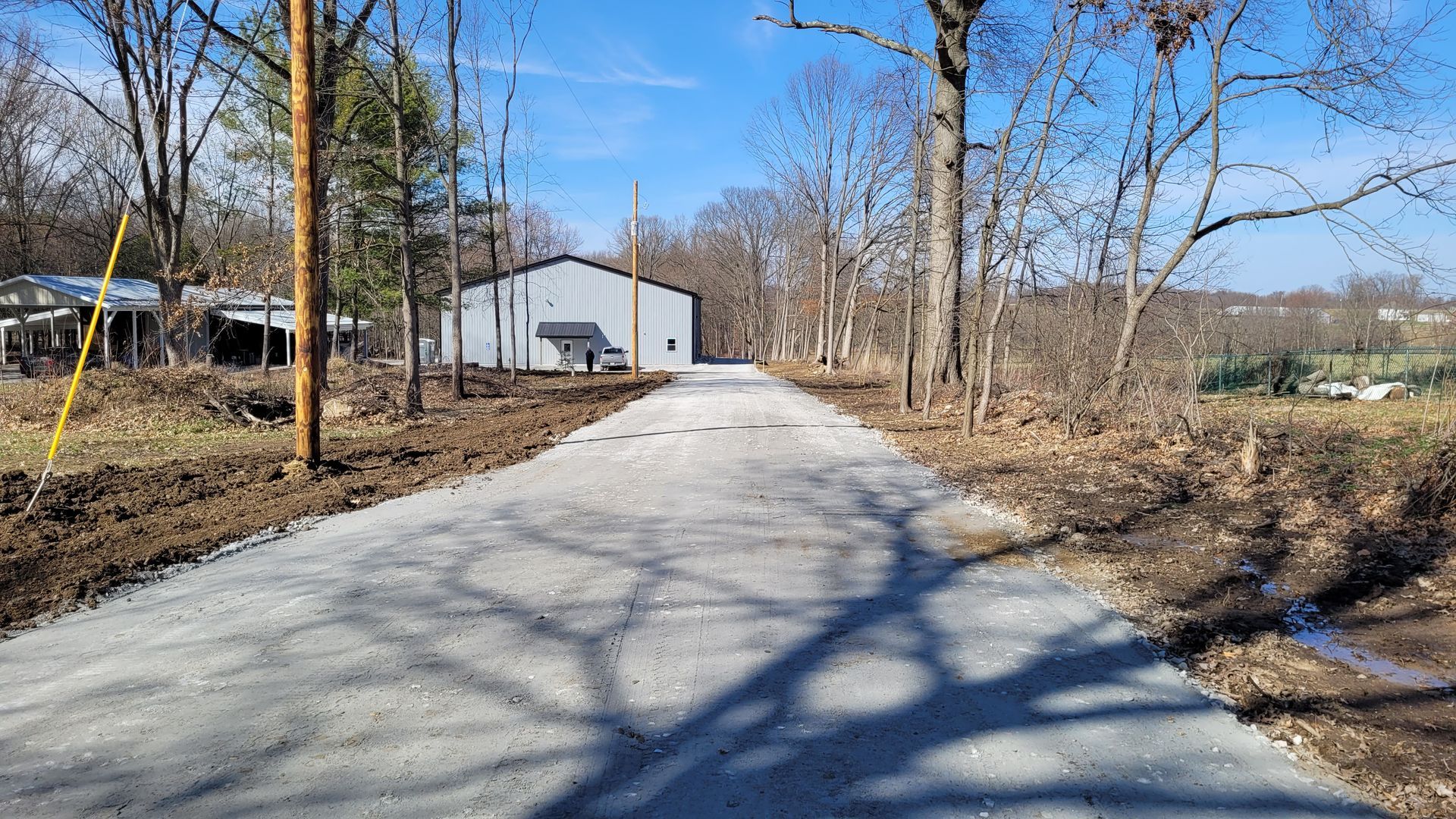 Gravel road leading to a metal building flanked by trees on a sunny day.