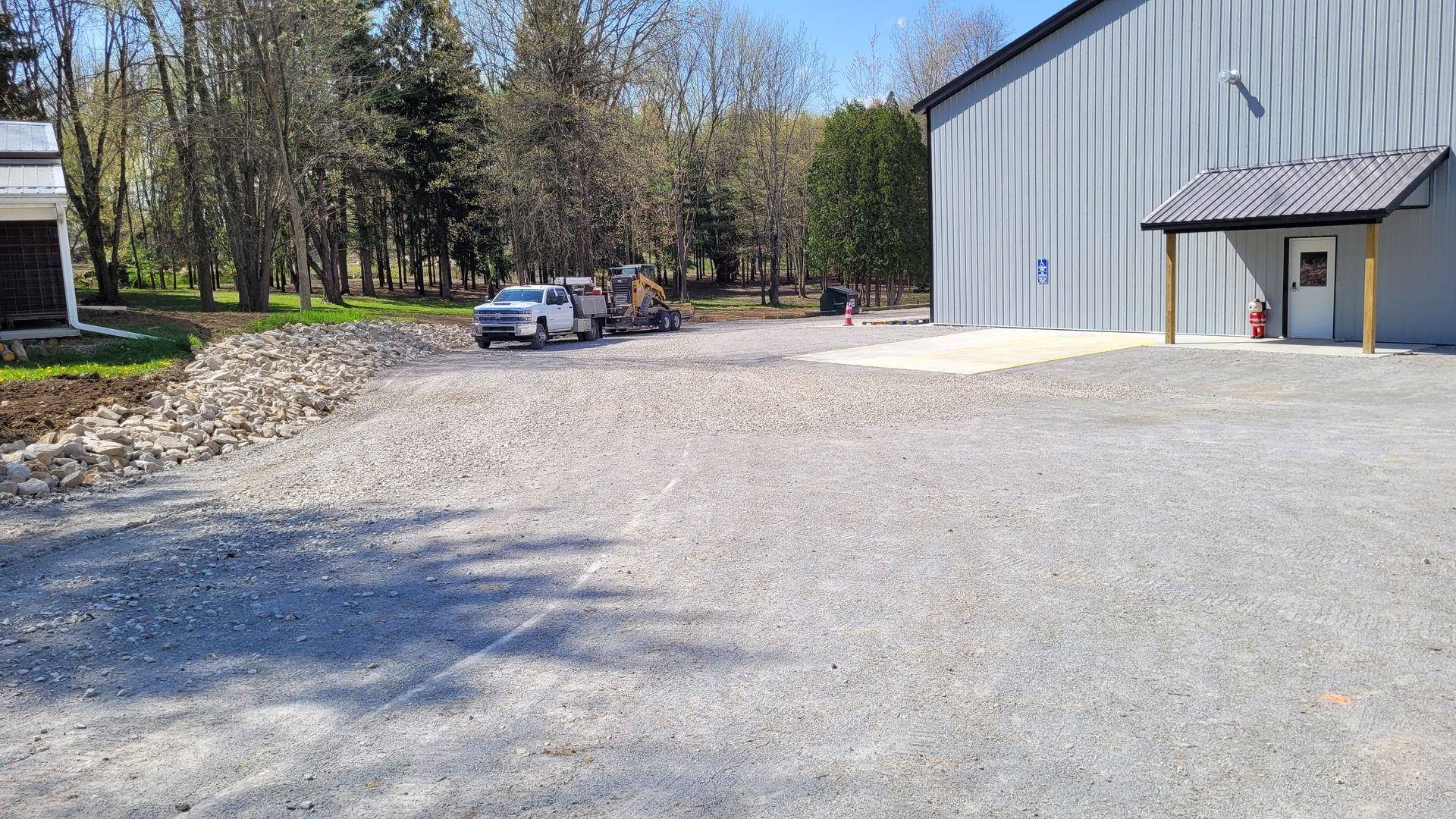 Gravel parking area next to a large metal building with a small canopy. A pickup truck and equipment are parked.