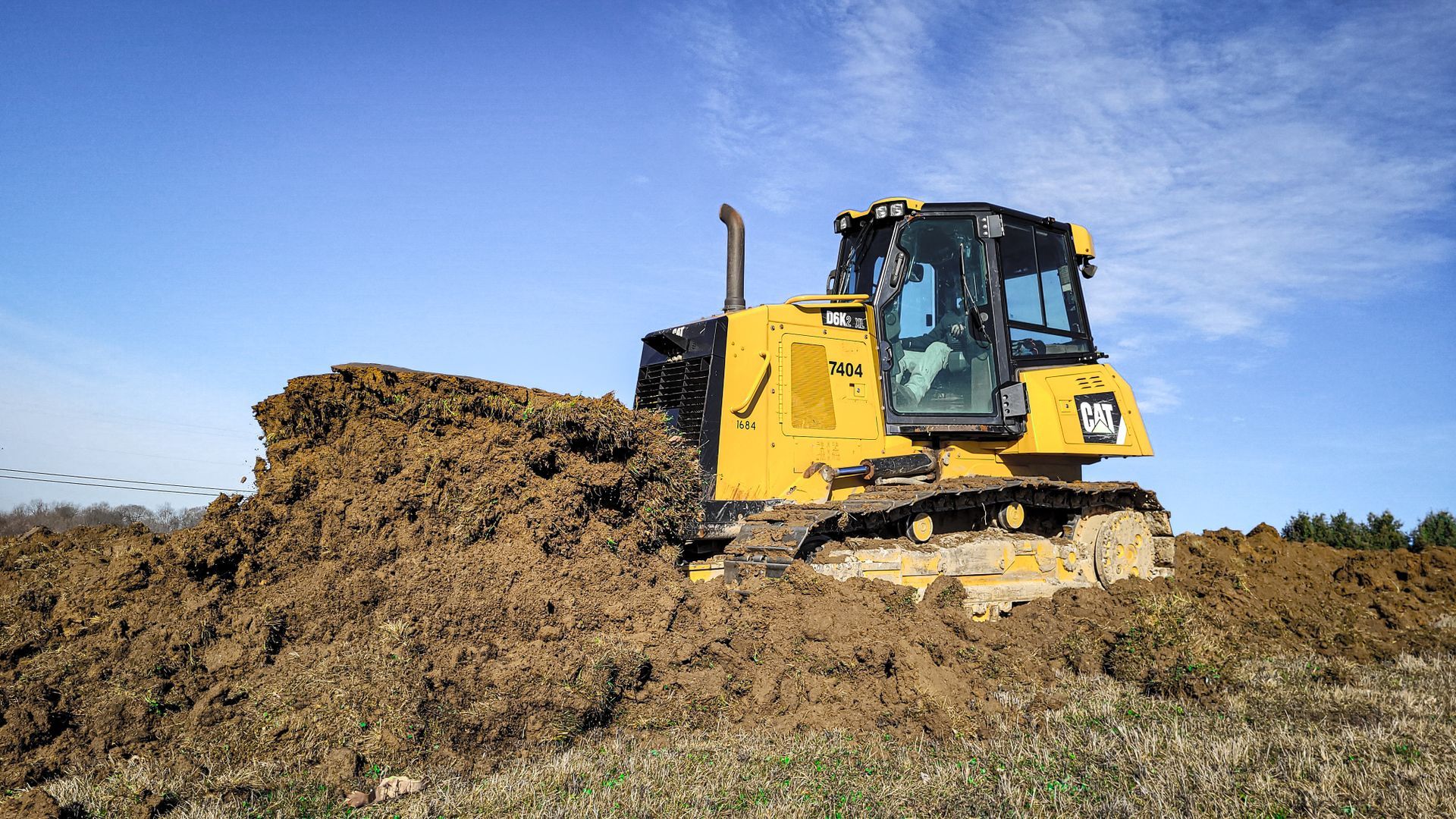 Yellow bulldozer pushing a pile of dirt across a field under a blue sky.