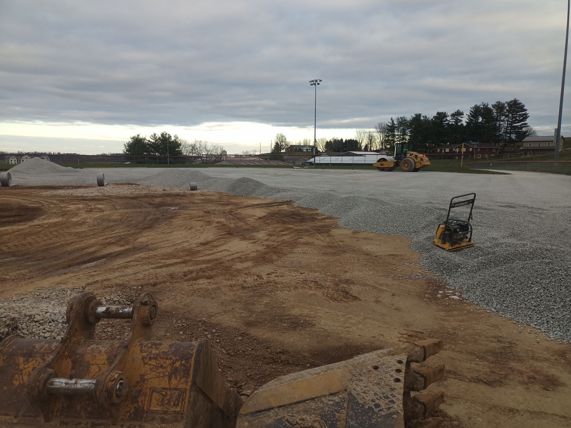 Construction site with gravel and sand, heavy machinery, cloudy sky.