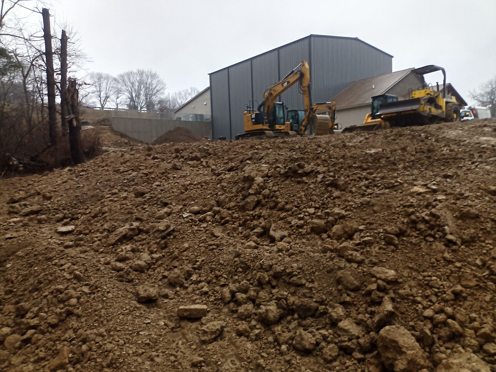 Construction site with excavator and bulldozer on a mound of dirt in front of a building.
