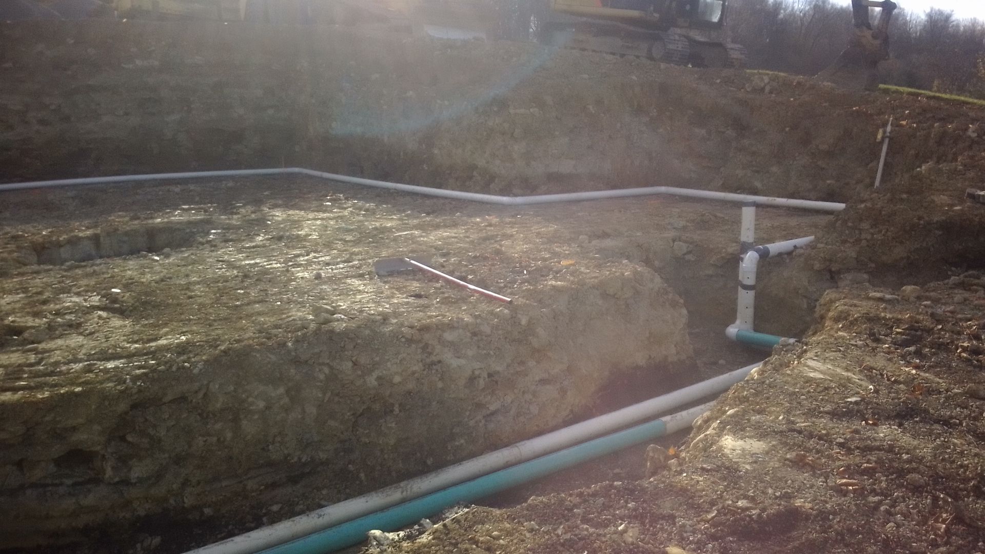 Construction site with exposed ground and pipes in trenches. White and green pipes are laid in the soil.