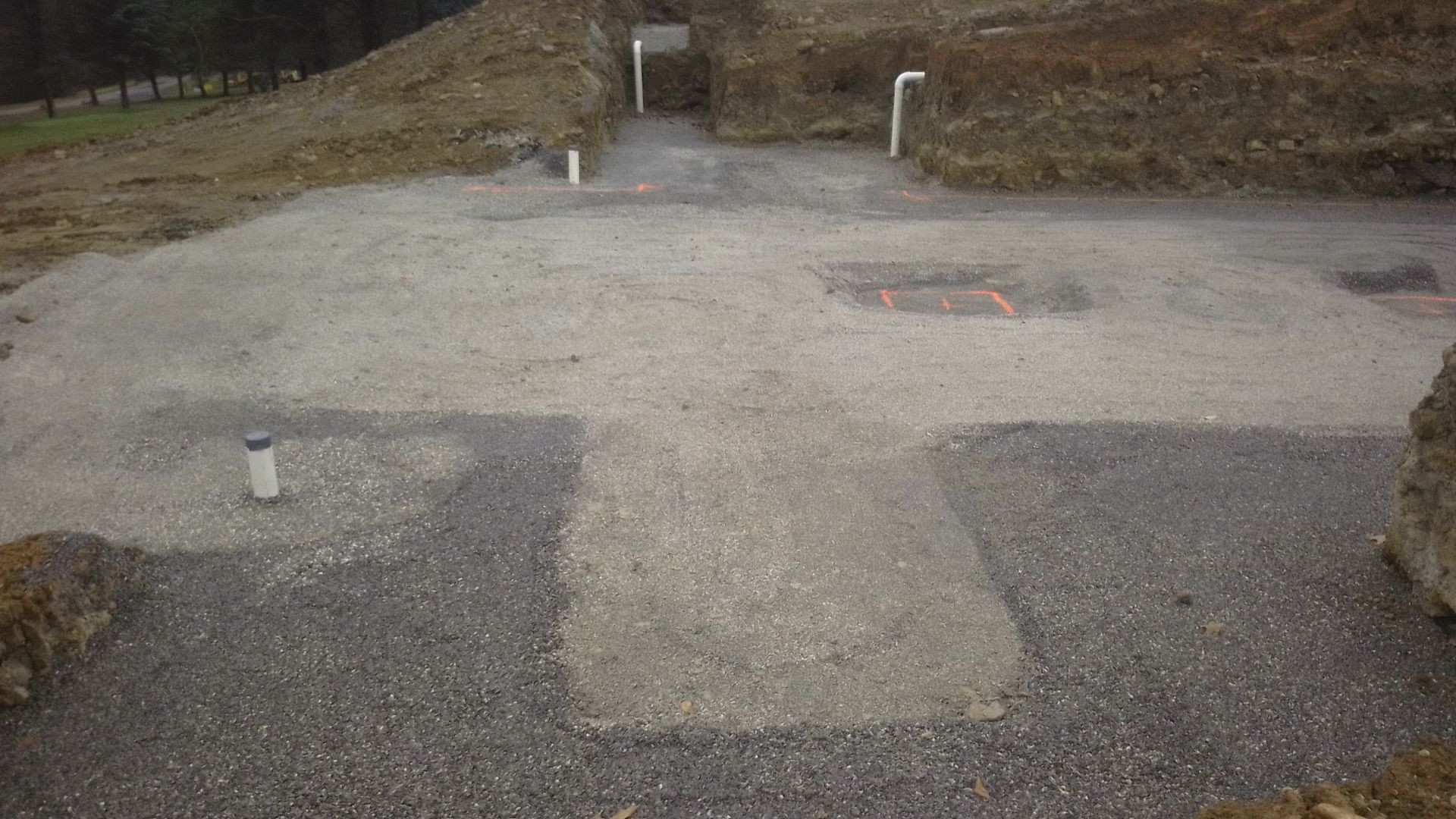 Gravel surface with buried utilities, surrounded by dirt and a grassy hill in the background.