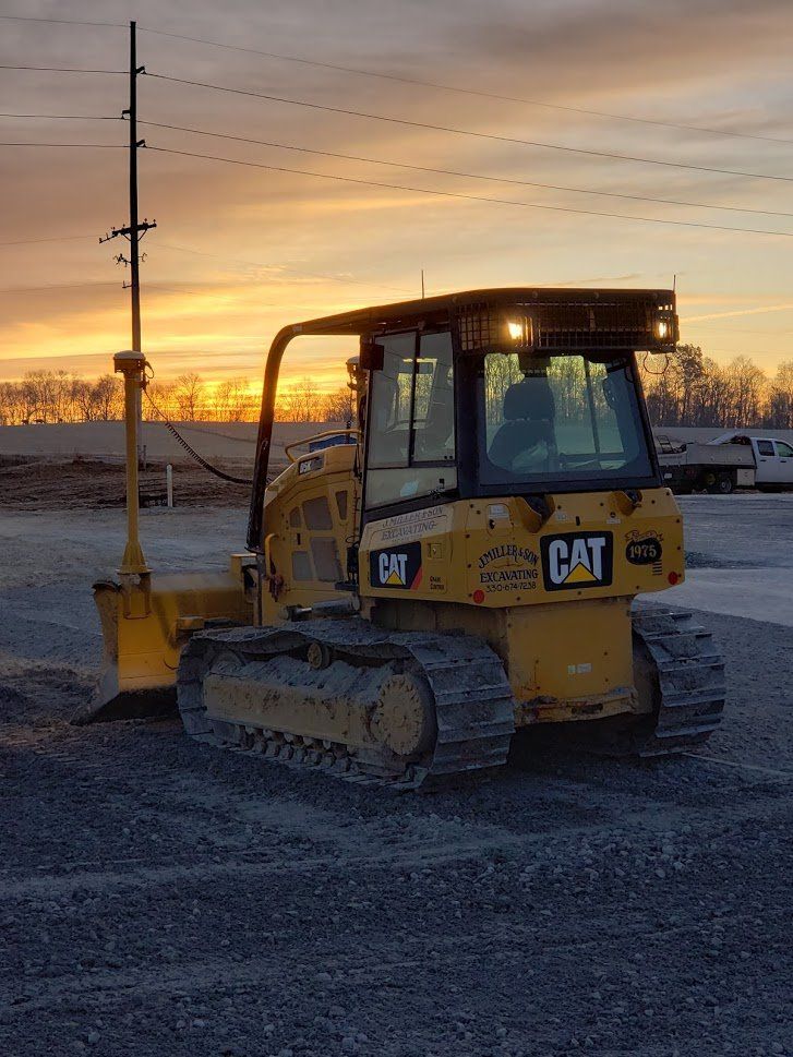 Yellow CAT bulldozer on gravel, with a sunrise in the background. It has a tall pole on the side.