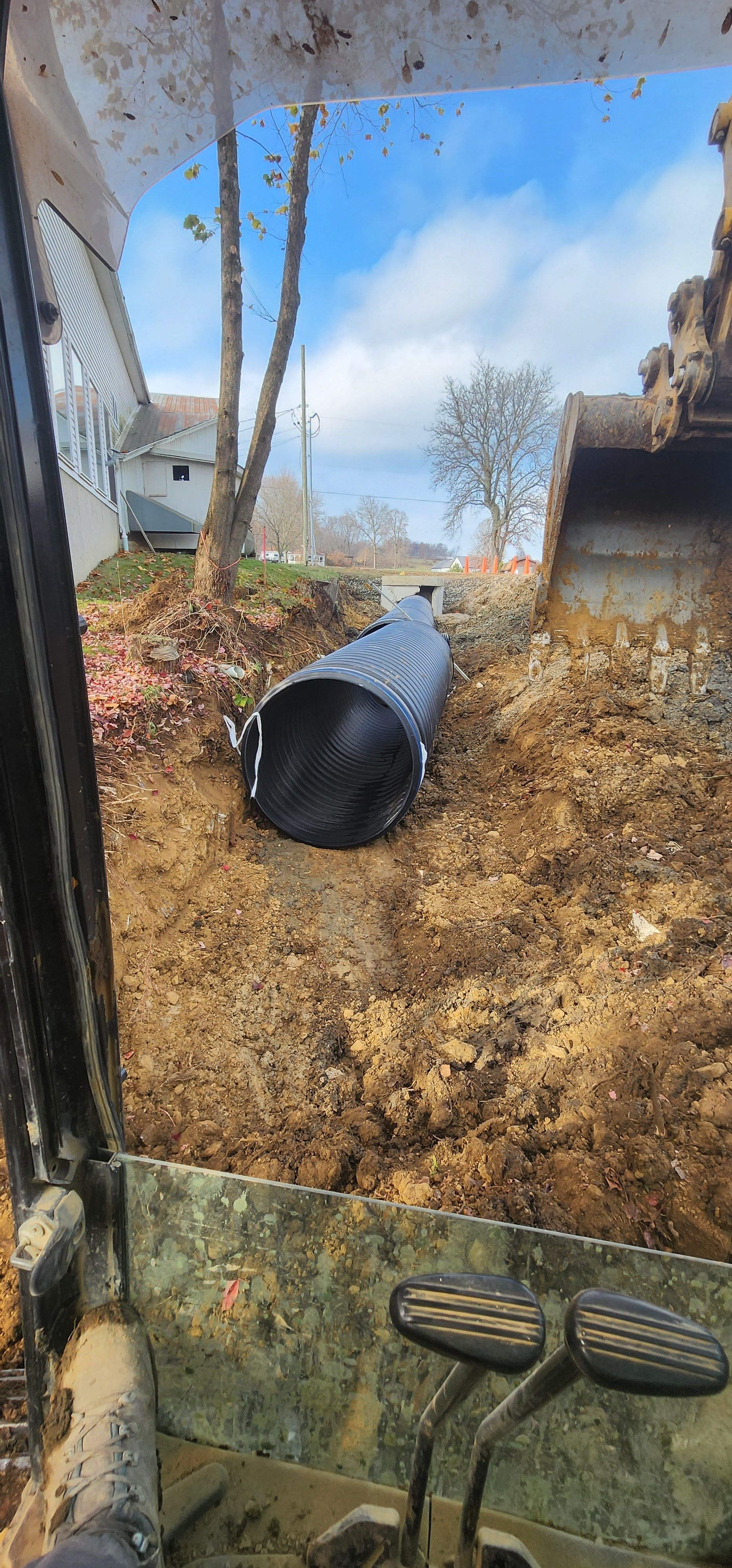 View from an excavator of a black drainage pipe laid in a trench on a hillside.