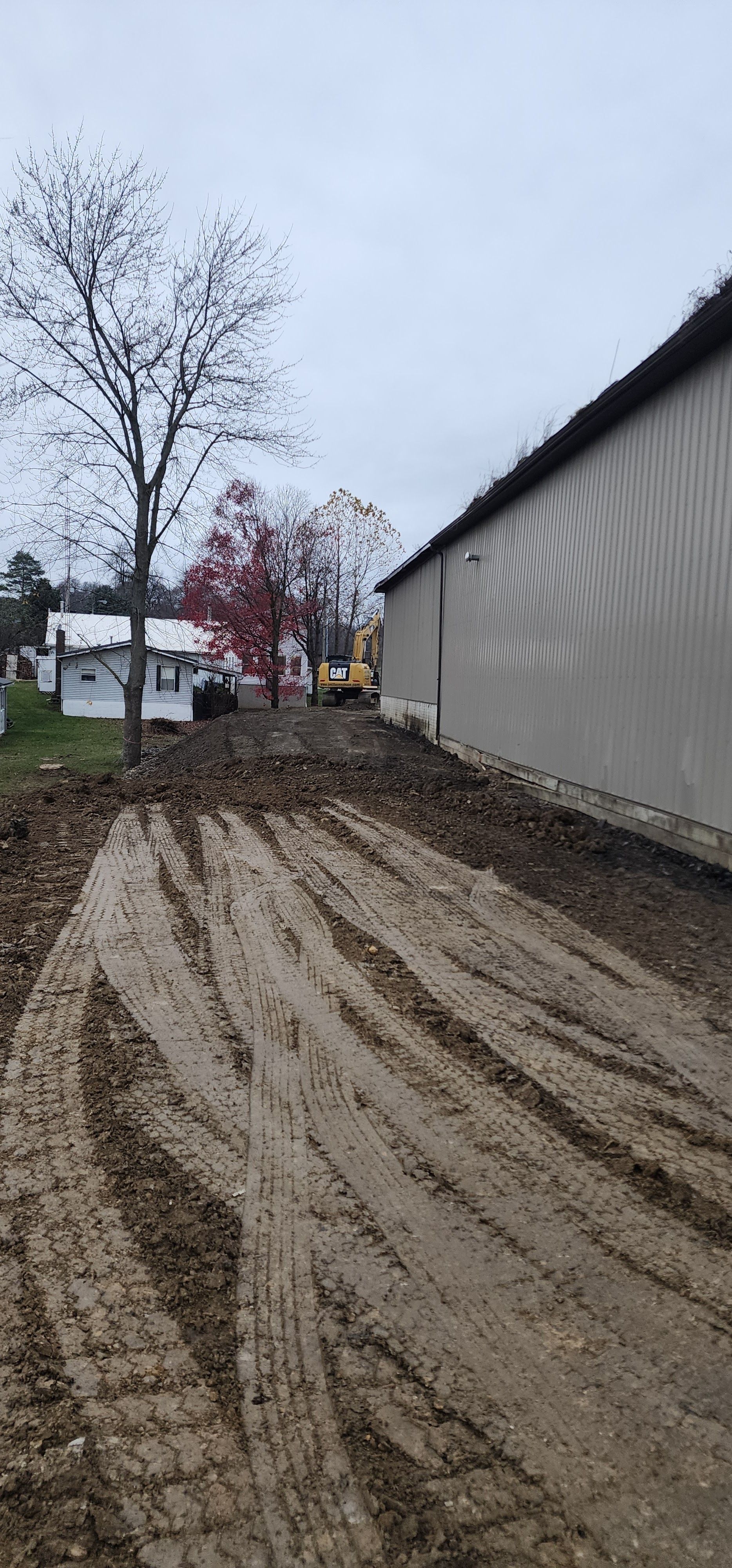 Muddy ground with tire tracks. A building is on the right, and trees are in the background. Cloudy day.