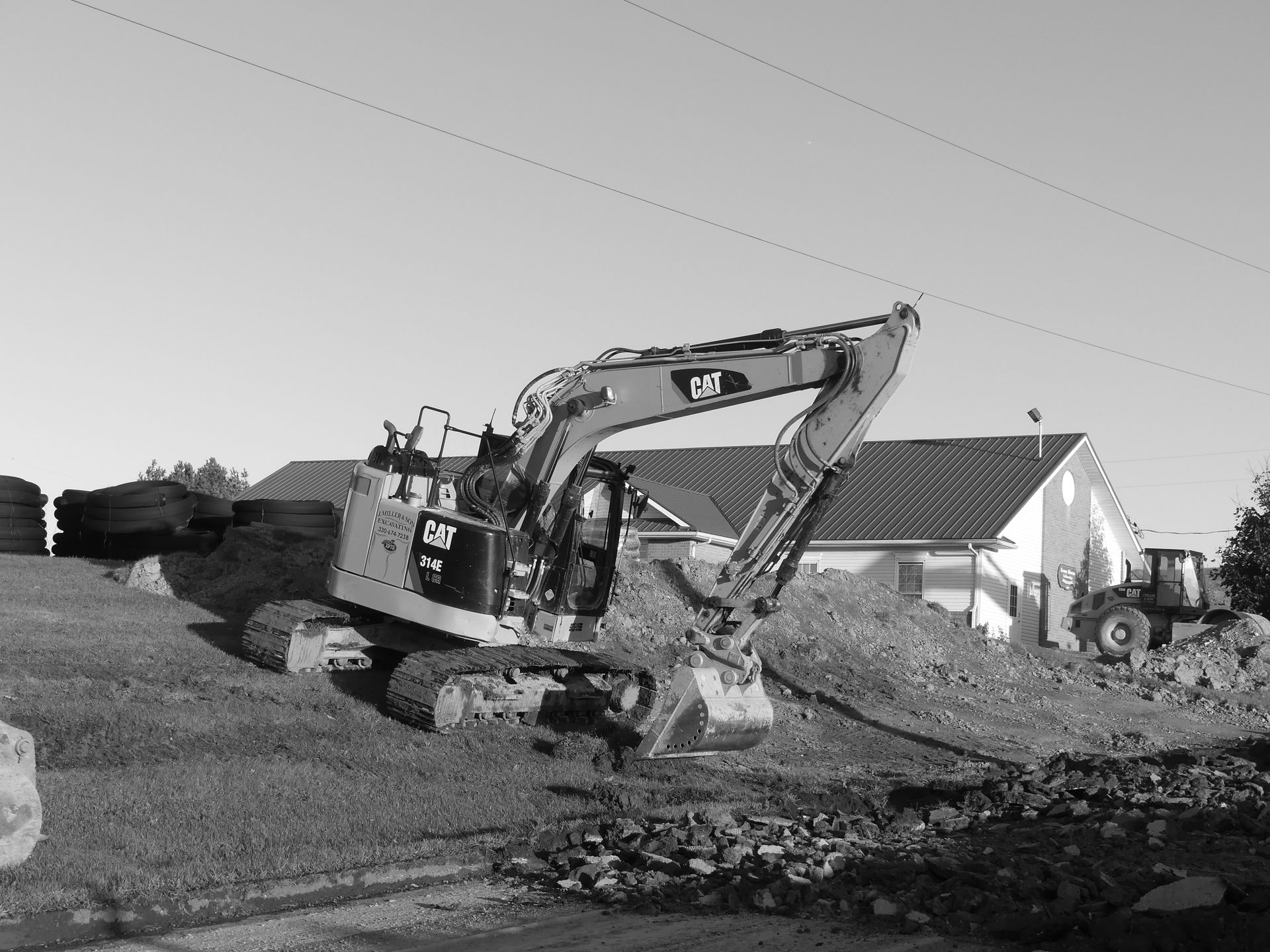 Excavator on a construction site, scooping dirt next to a building on a sunny day.