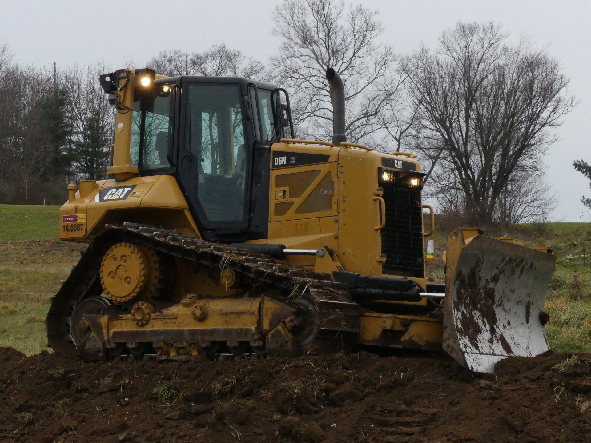 Yellow Caterpillar bulldozer on muddy ground, pushing soil.