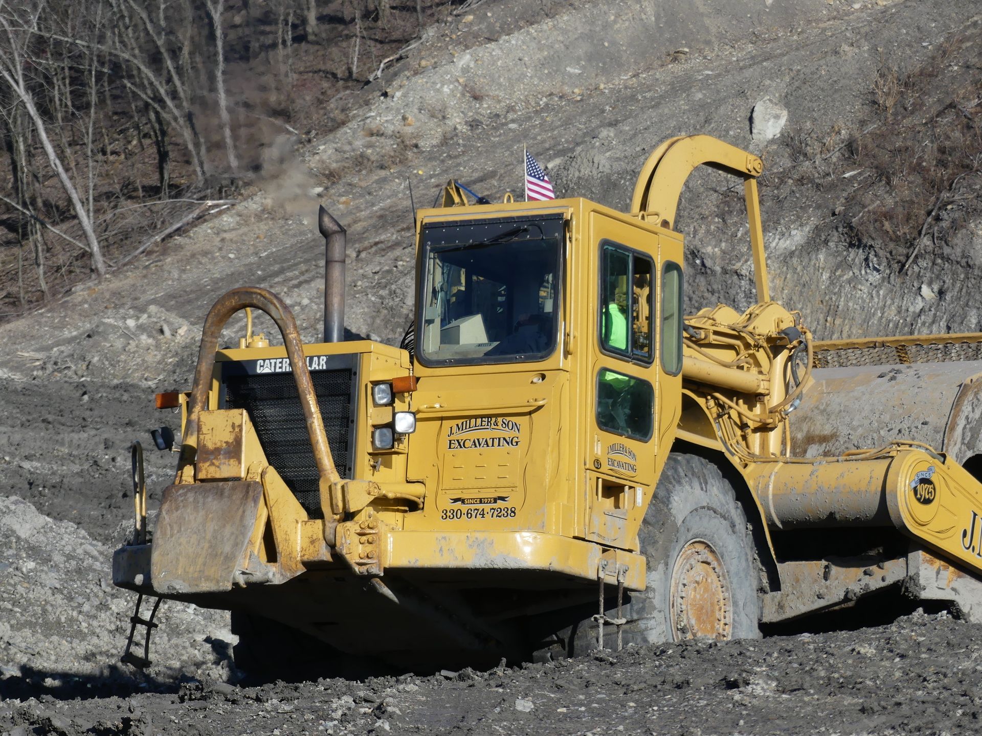 Yellow Caterpillar construction machine grading earth on a hillside.
