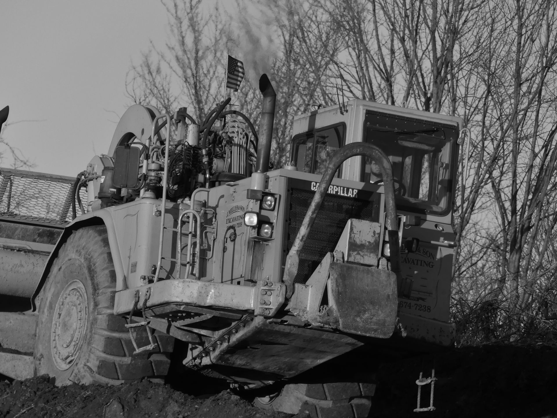 Yellow industrial vehicle outdoors near trees, with smoke rising.