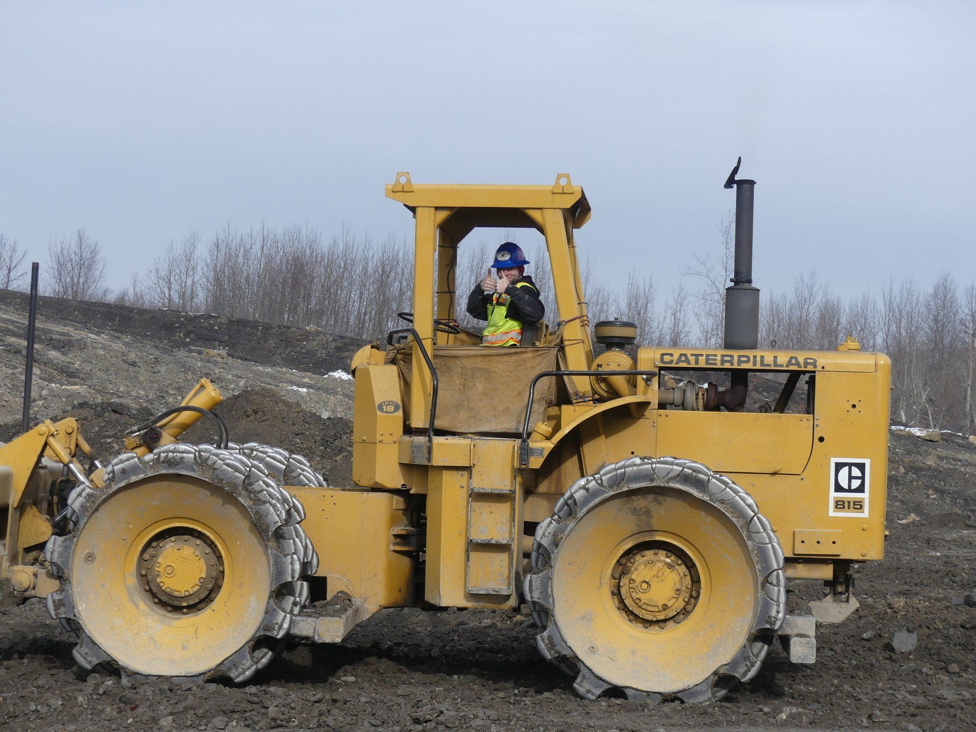 Yellow Caterpillar compactor with a driver at a construction site.