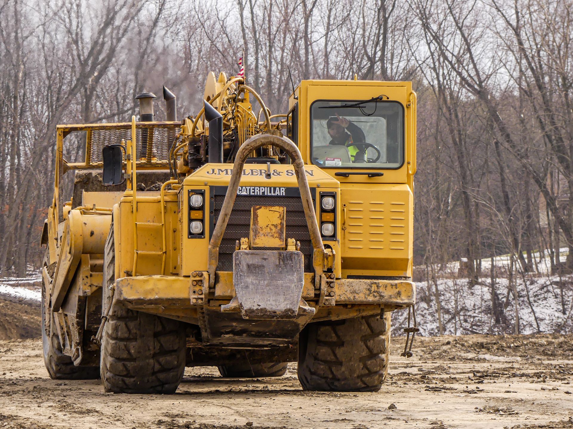 Yellow construction machine on muddy ground, with driver in the cab.