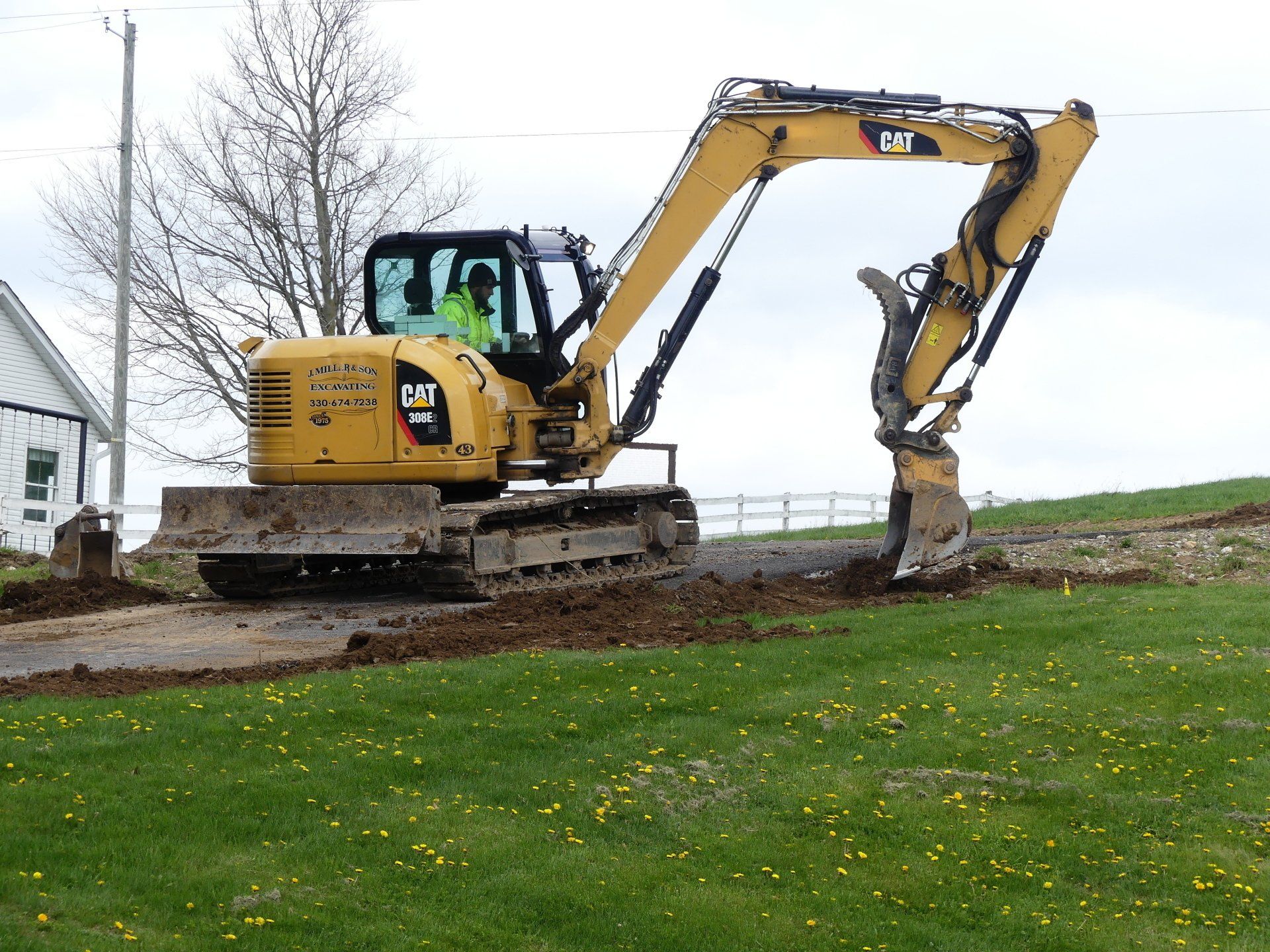 Yellow excavator digging a trench on a grassy area, with an operator inside.